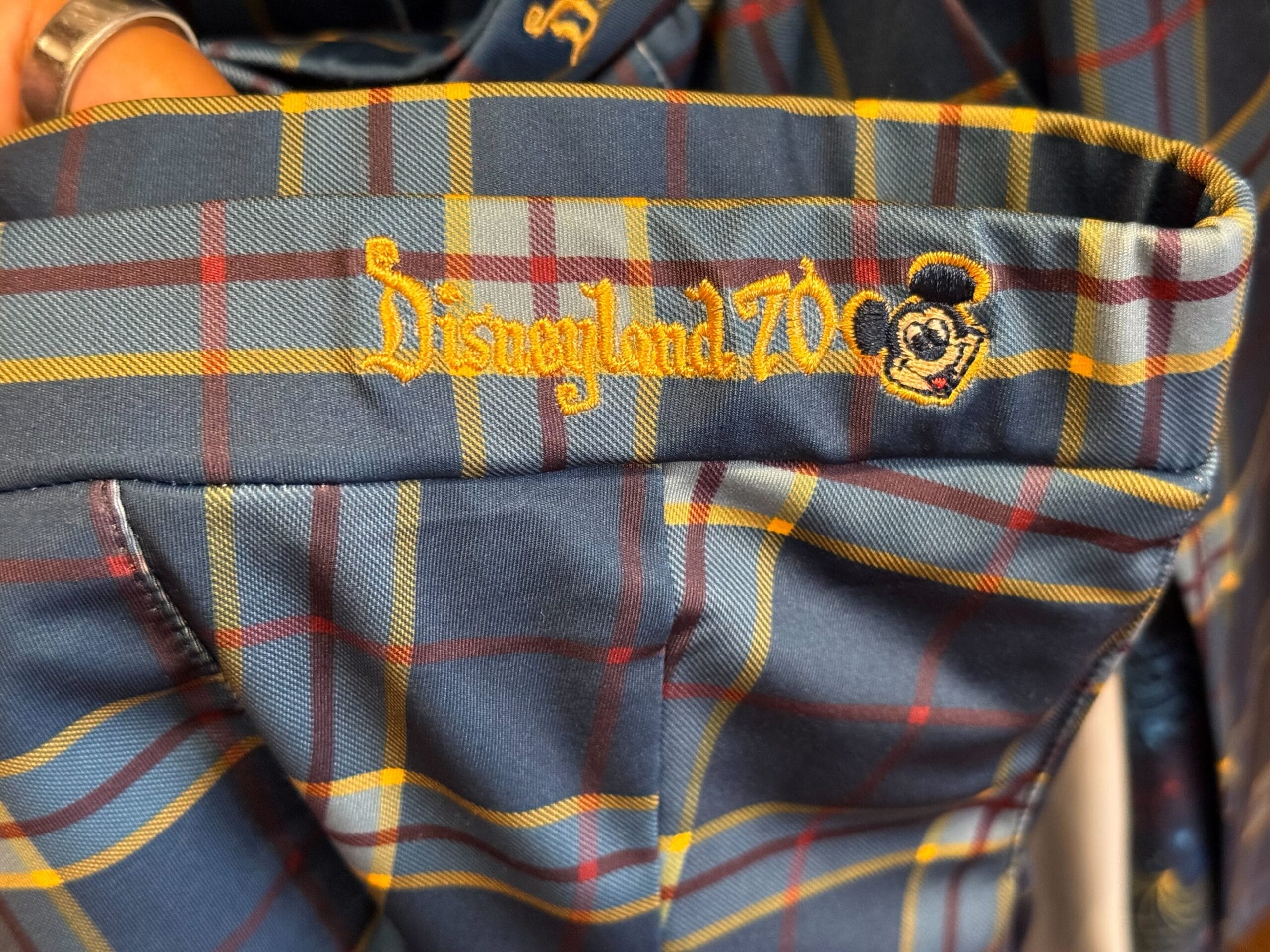 Close-up of blue plaid fabric with "Disneyland 70" and a yellow Mickey Mouse face, celebrating Disneyland's milestone anniversary.