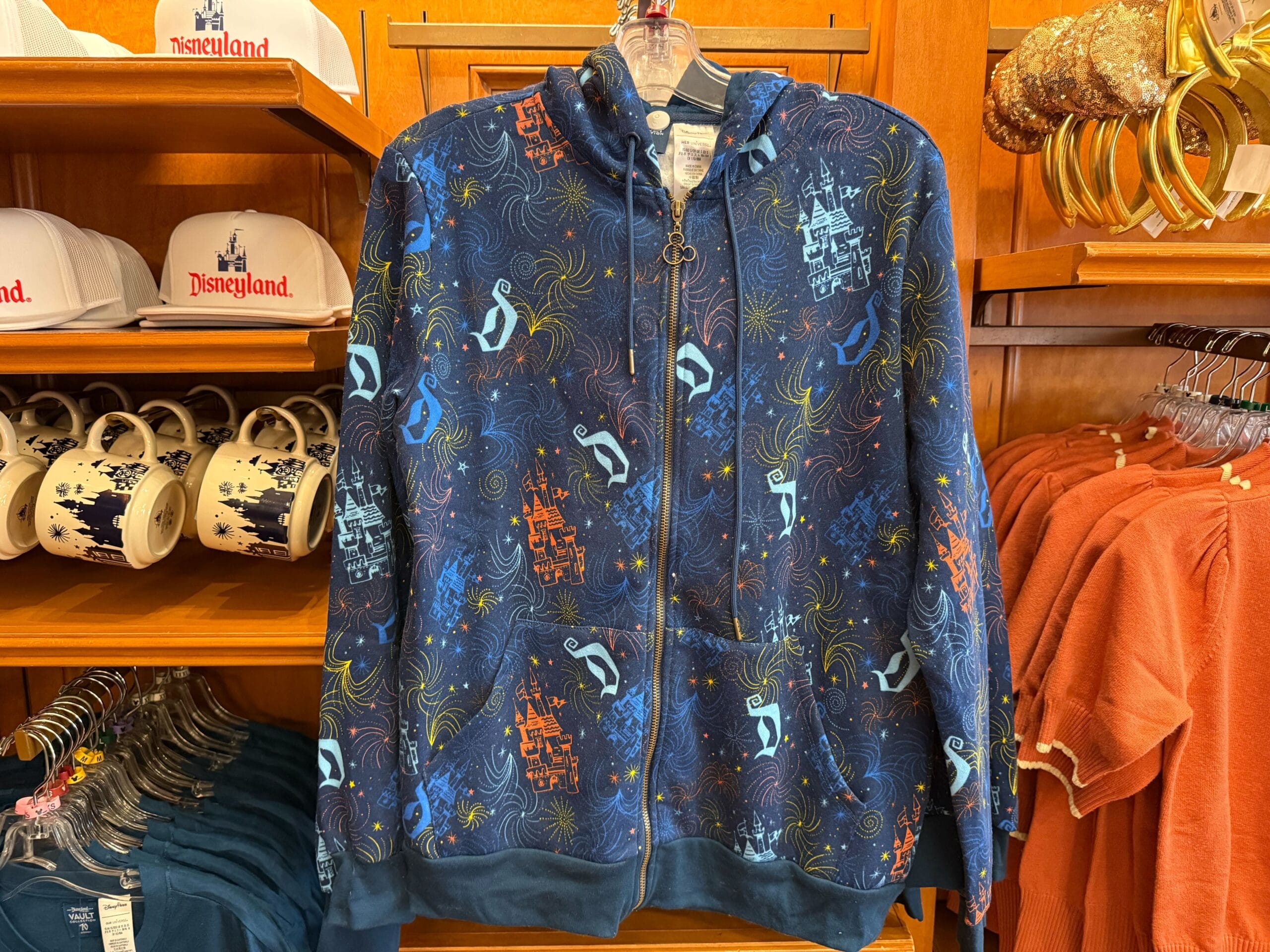 Navy blue Disneyland jacket featuring a castle like Sleeping Beauty Castle, "D", and fireworks, on a rack with more park merch.