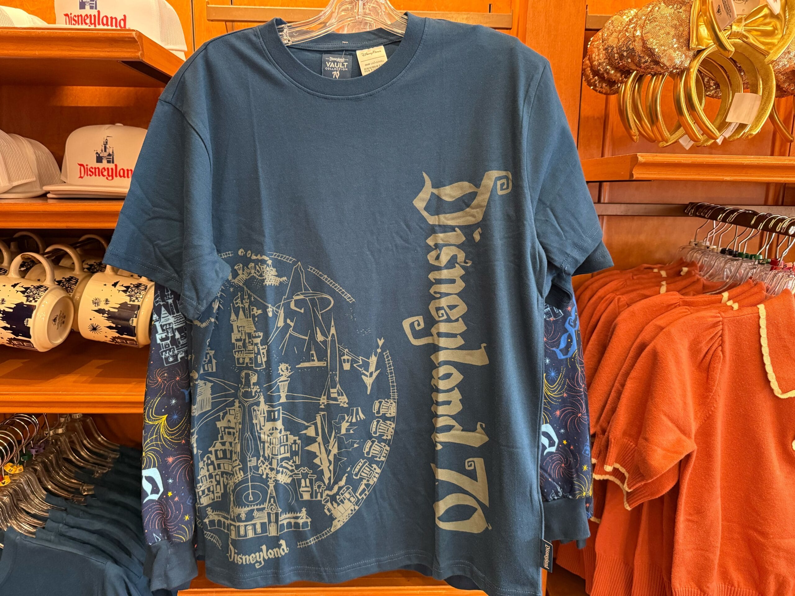 Navy blue Disneyland 70th anniversary shirt with gold lettering and a map graphic featuring Sleeping Beauty Castle, in a gift shop.