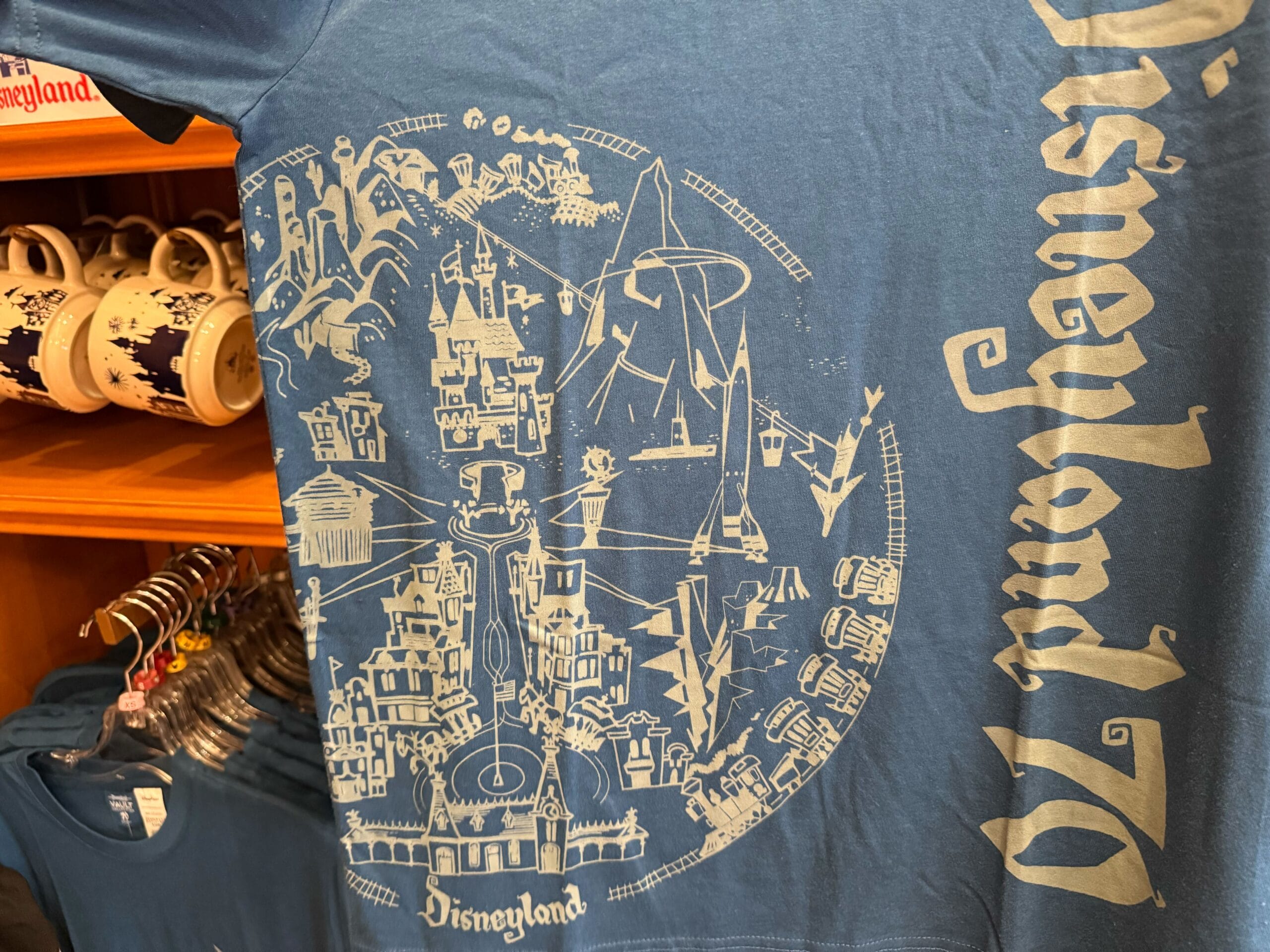 Blue Disneyland 70th tee features white line art of park icons and “Disneyland” text—castle resembles Anaheim’s, not Cinderella Castle.