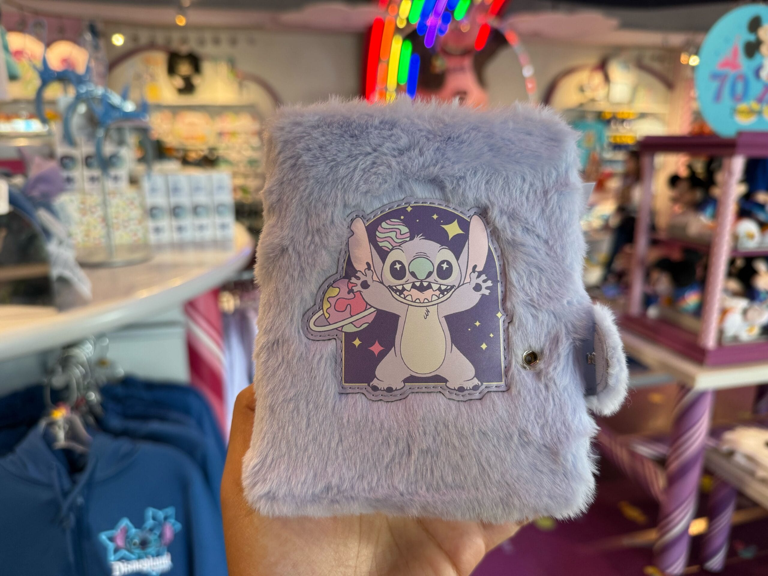 A hand holds a Fluffy Stitch Journal at Disneyland in a bright, happy shop, perfect for park memories—no castle visible here.