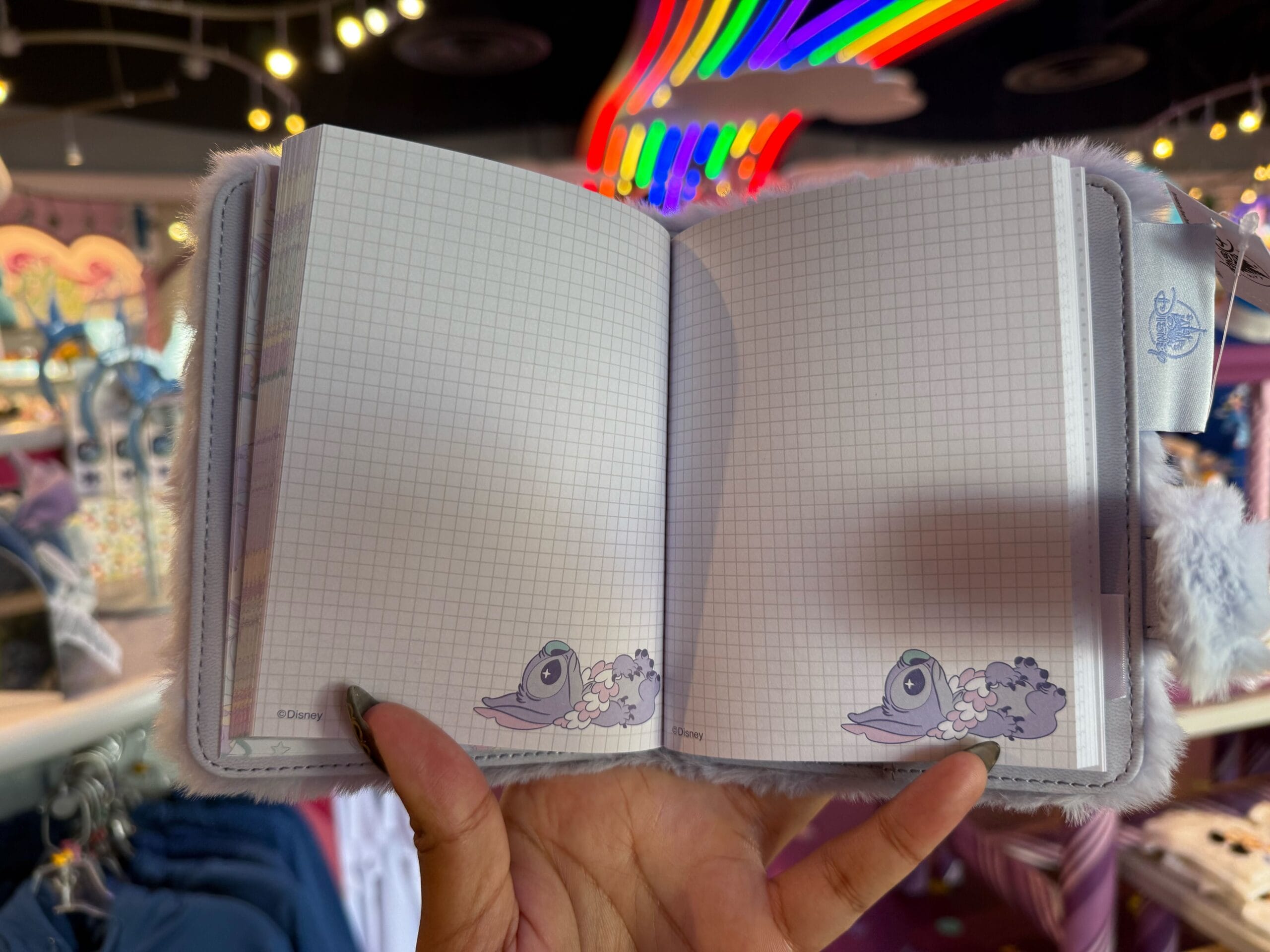 Person holding a Fluffy Stitch Journal with sea creatures, under Disneyland-style lights, evoking a magical park atmosphere.