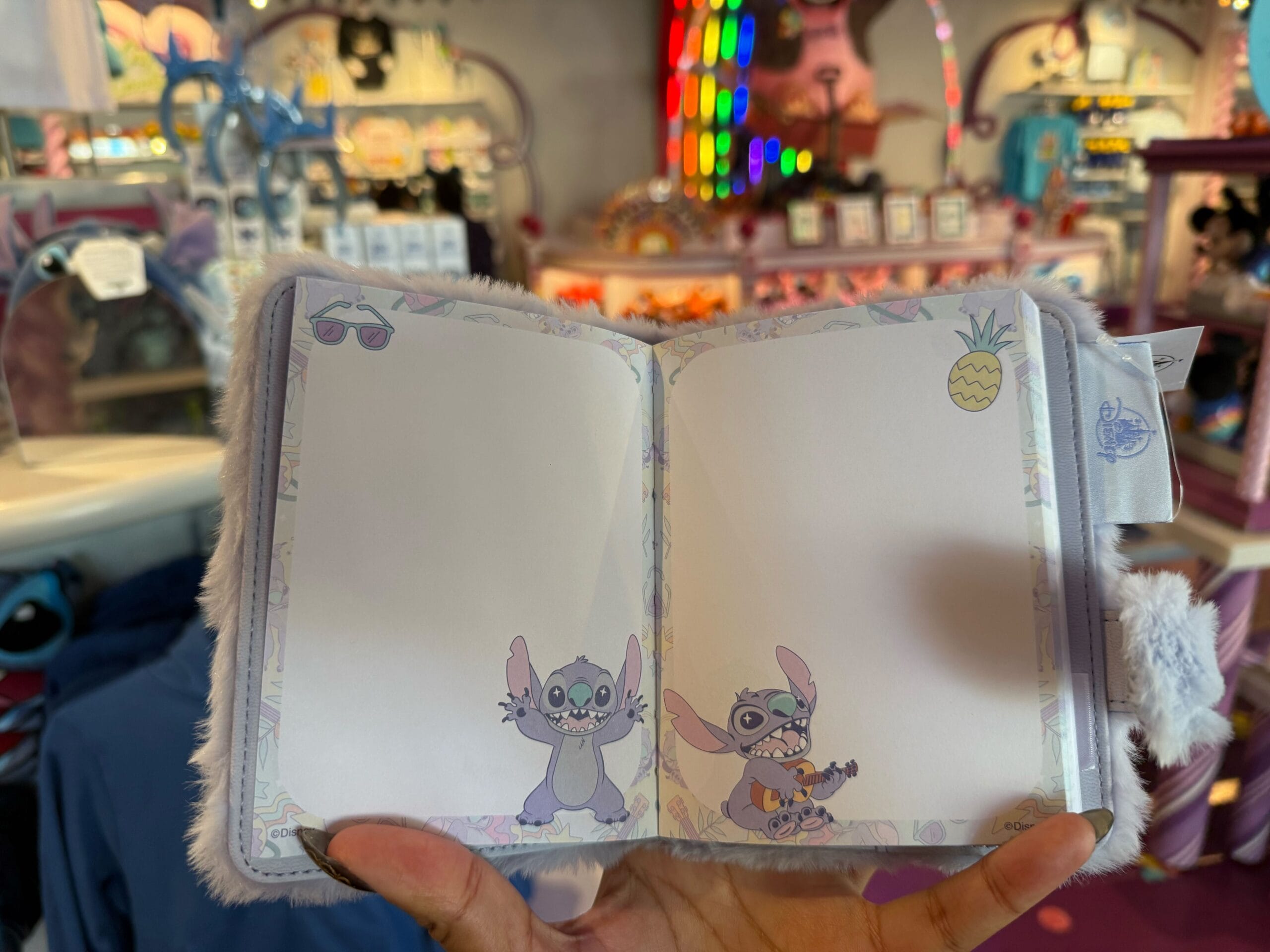A plush Stitch journal for capturing memories, displayed in a vibrant Disney park shop stocked with playful Stitch merchandise.