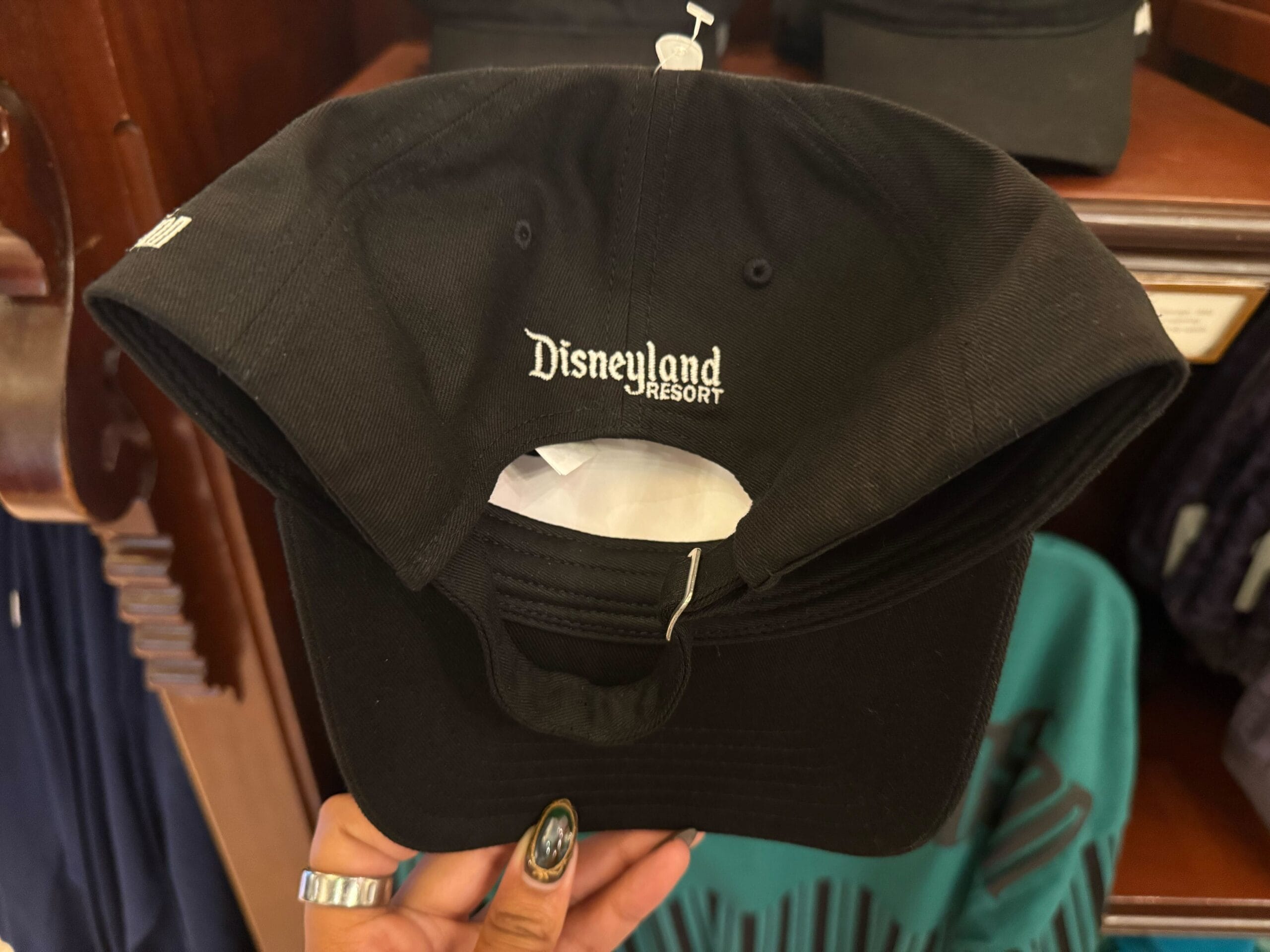 A hand holds a black hat with "Disneyland Resort" in white on the back, a souvenir unique to Disneyland’s original Anaheim park.