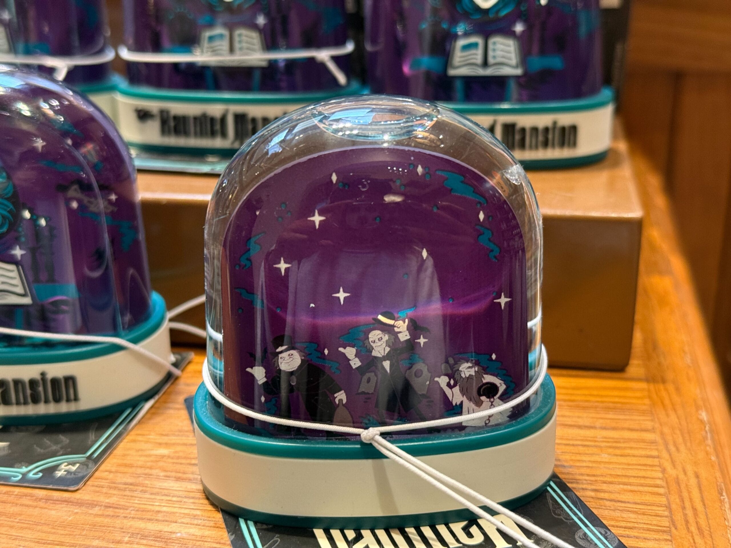 Disney Parks' Haunted Mansion-inspired purple snow globe with three ghost figures, displayed on a wooden shelf; no castle present.