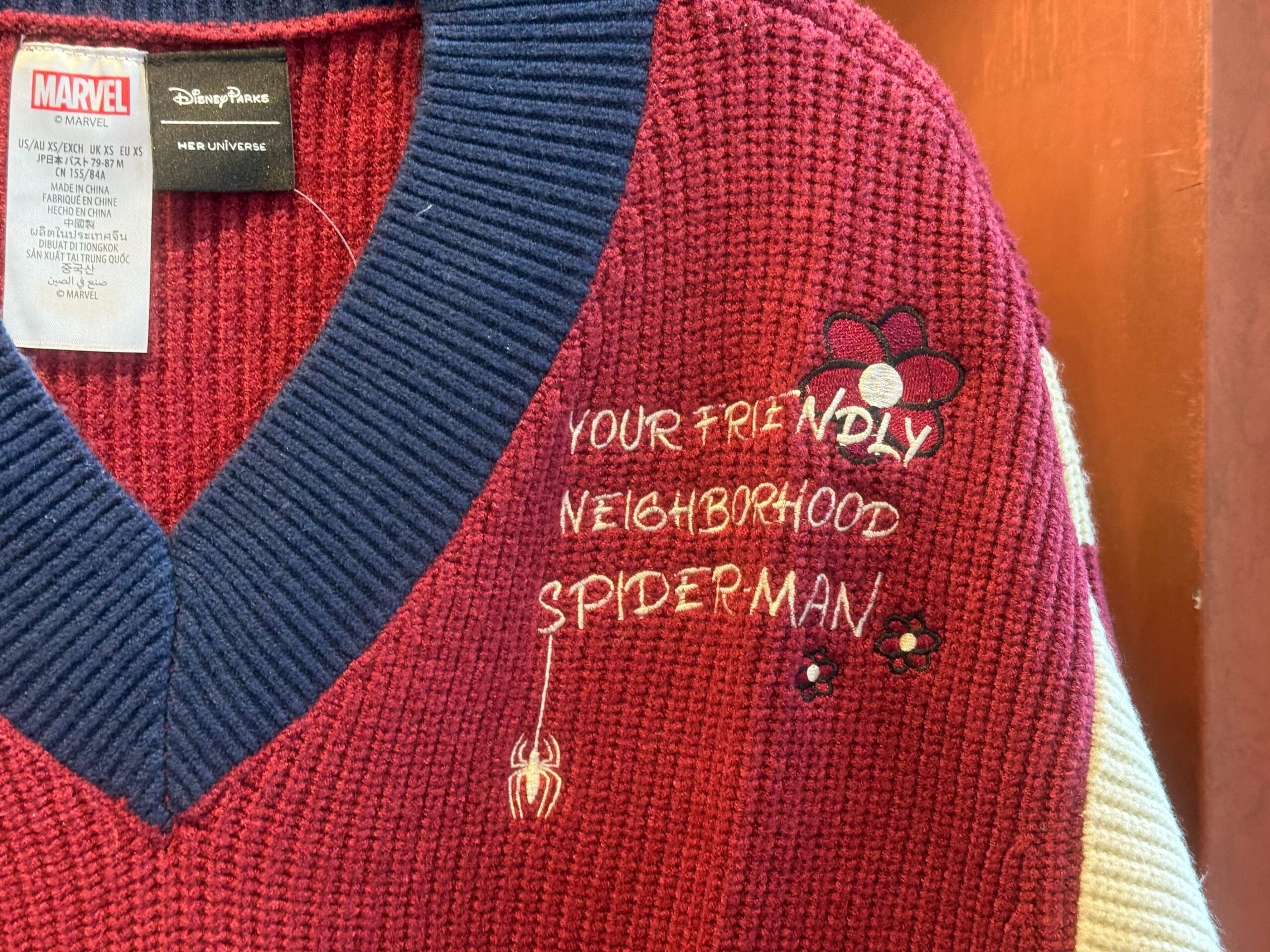Red knit sweater with navy collar, floral designs, and "Your Friendly Neighborhood Spiderman" embroidered, perfect for Disney park days.
