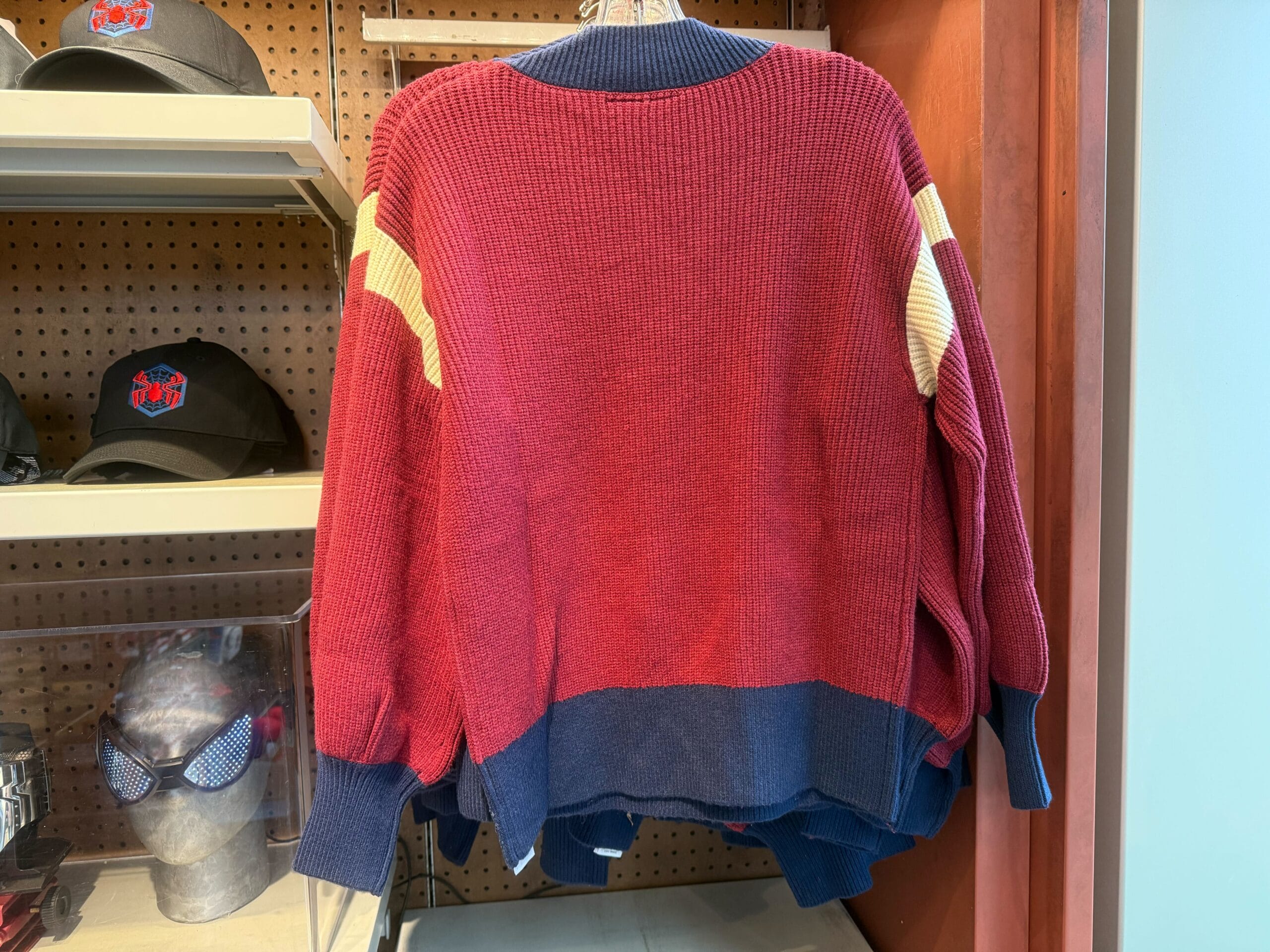 A red, blue, and cream colorblock sweater hangs on a rack in a shop, similar to apparel found in Main Street stores at Disney Parks.