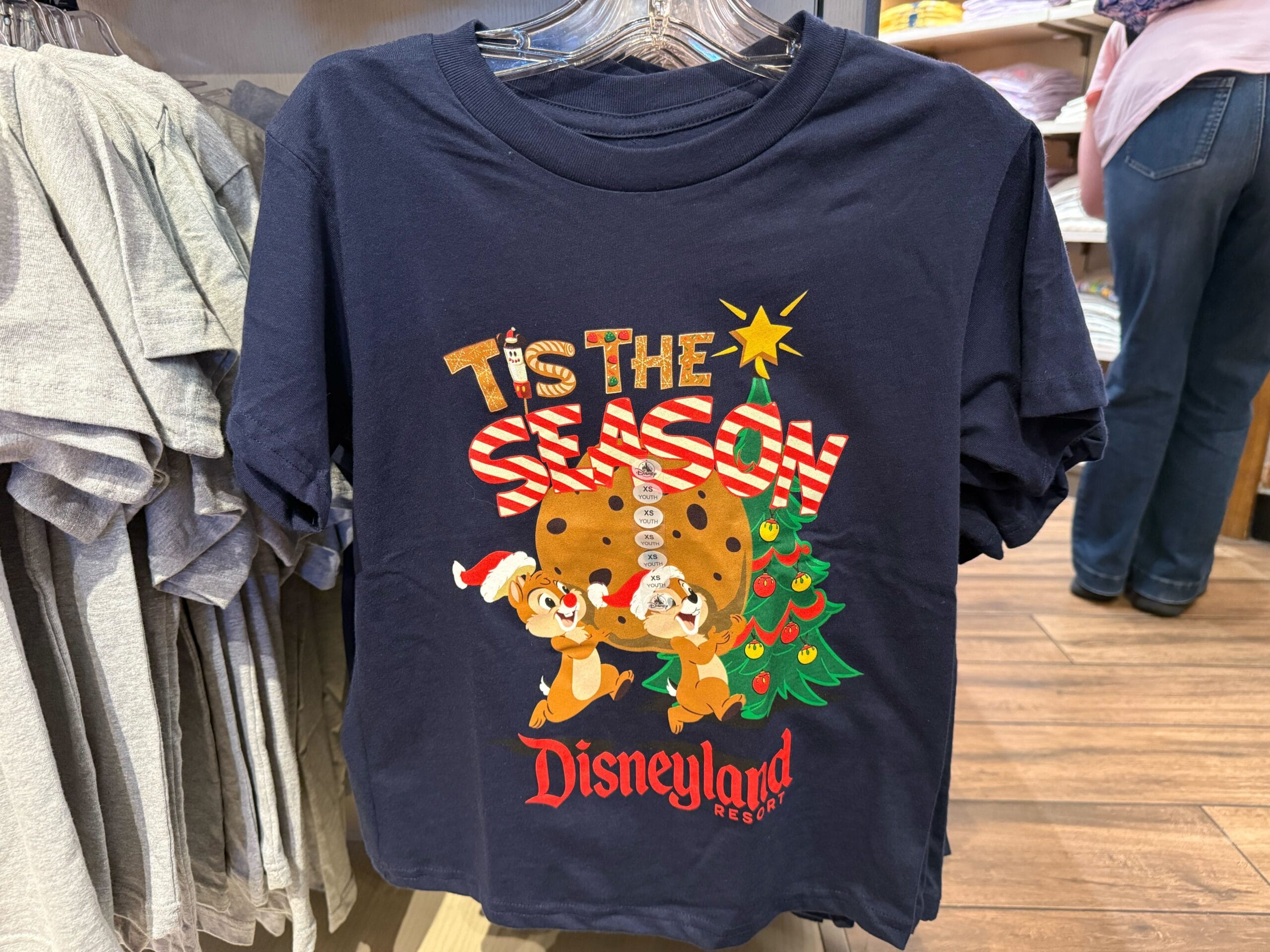 Navy Disneyland shirt featuring "’Tis the Season" and Chip and Dale in festive outfits by a Christmas tree and cookie; no castle shown.