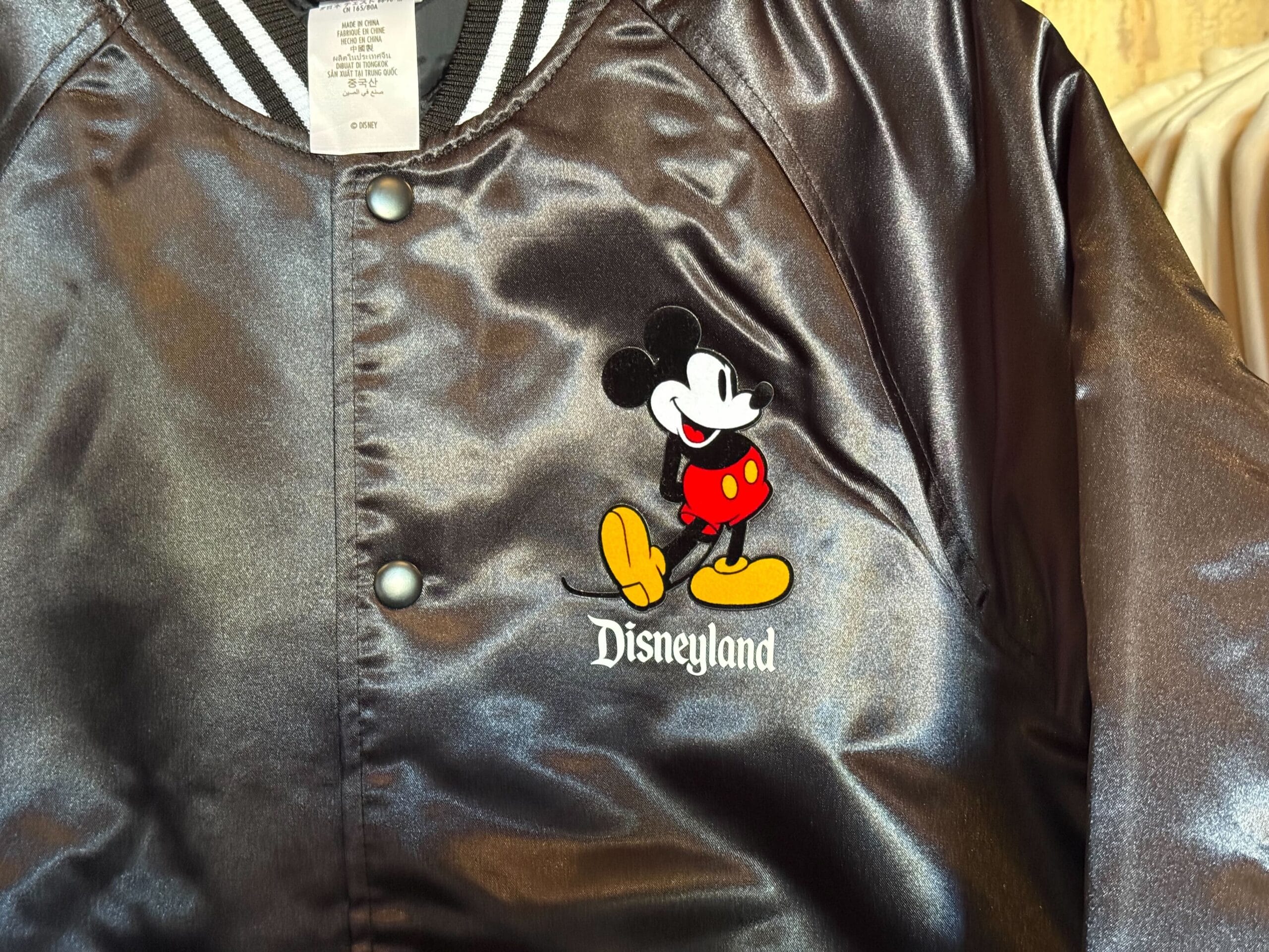 A glossy black jacket featuring Mickey Mouse and the word "Disneyland" on the front, reminiscent of classic Disney park apparel.