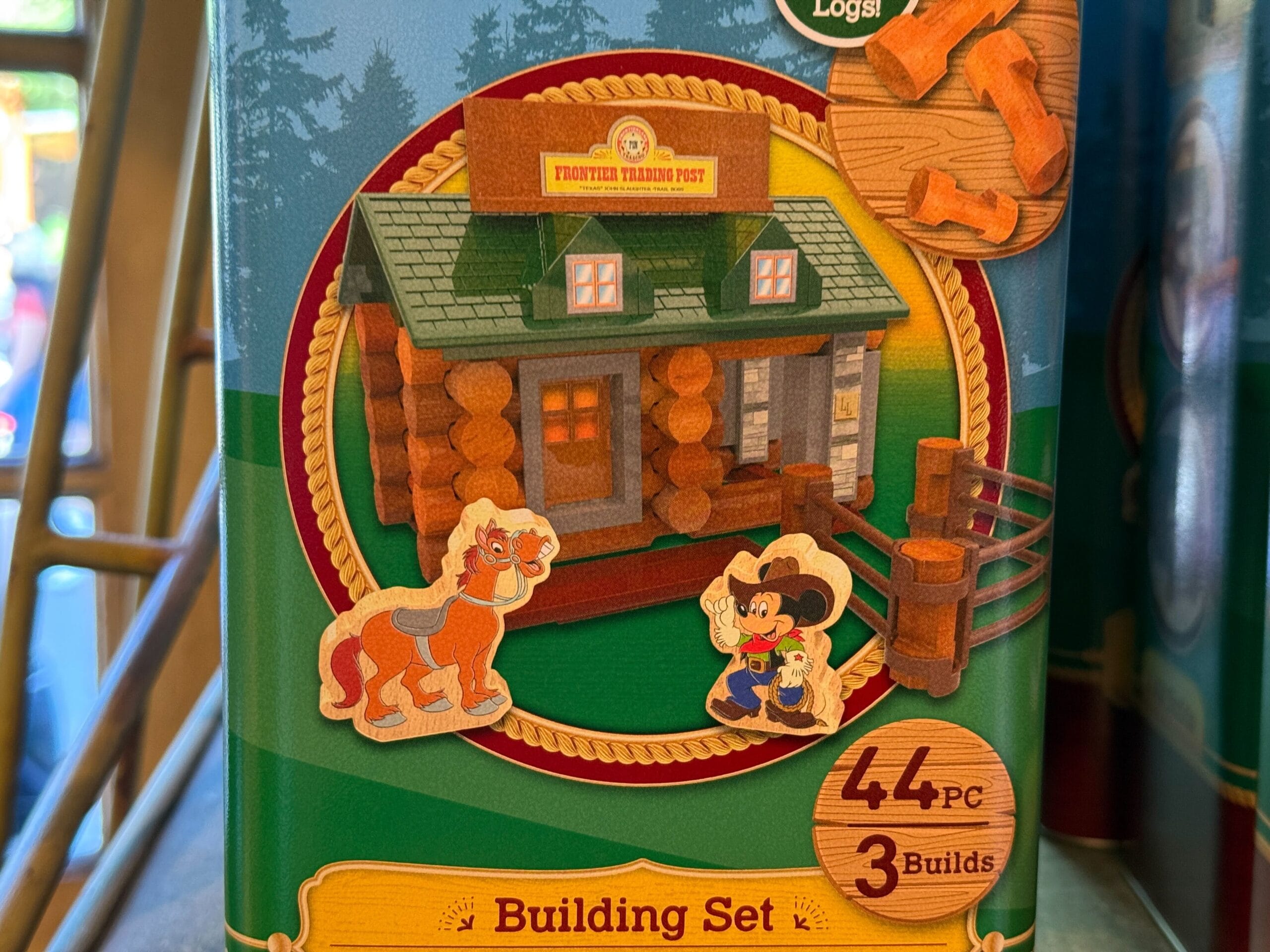 Toy log cabin building set box with 44 pieces, cartoon horse, cowboy, and dog shown in front of a frontier trading post.
