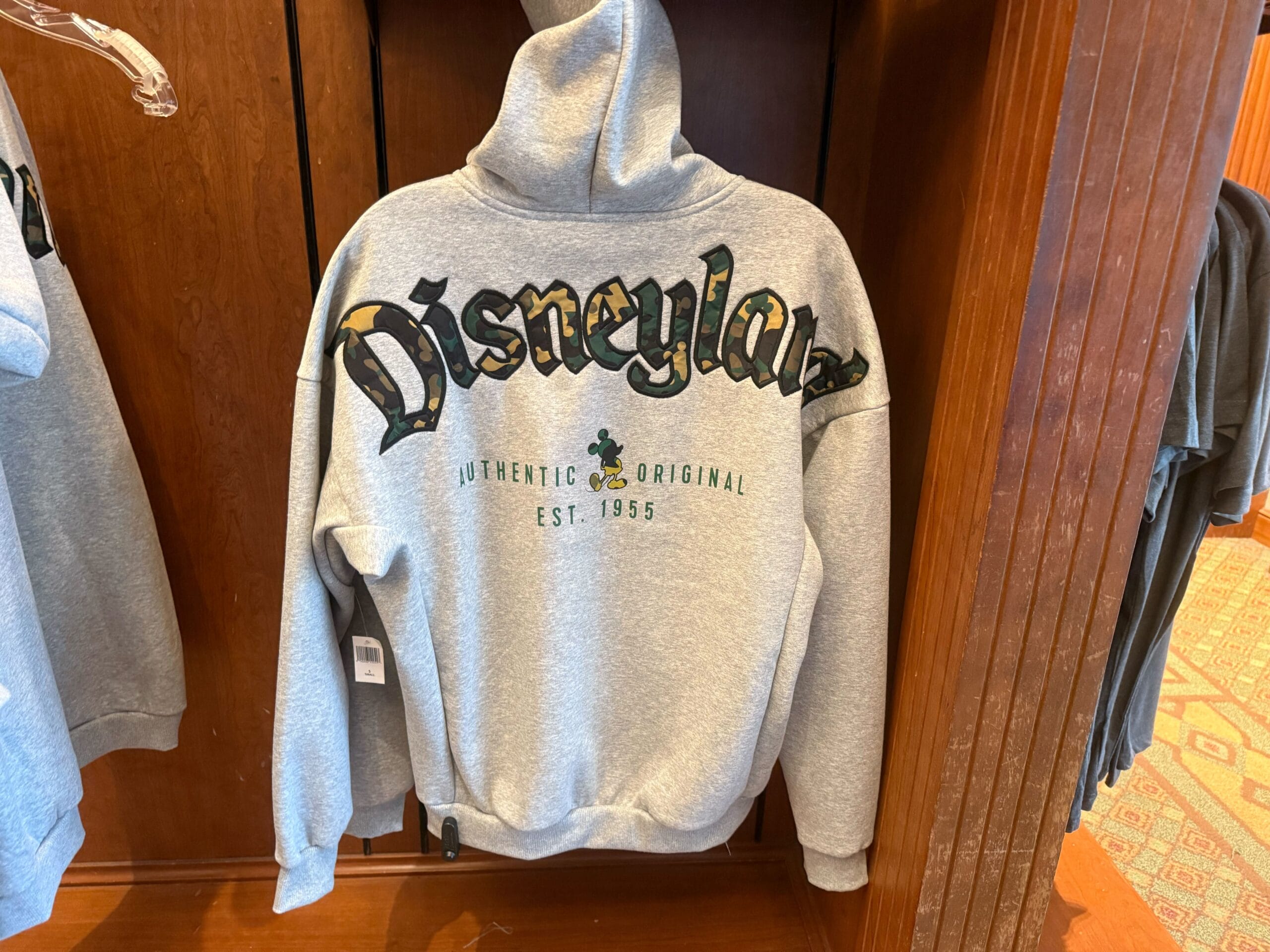 Back of gray Disneyland hoodie featuring bold Mickey camouflage print “Disneyland” lettering, plus “Authentic Original Est. 1955” on the back and a camouflage Mickey silhouette.
