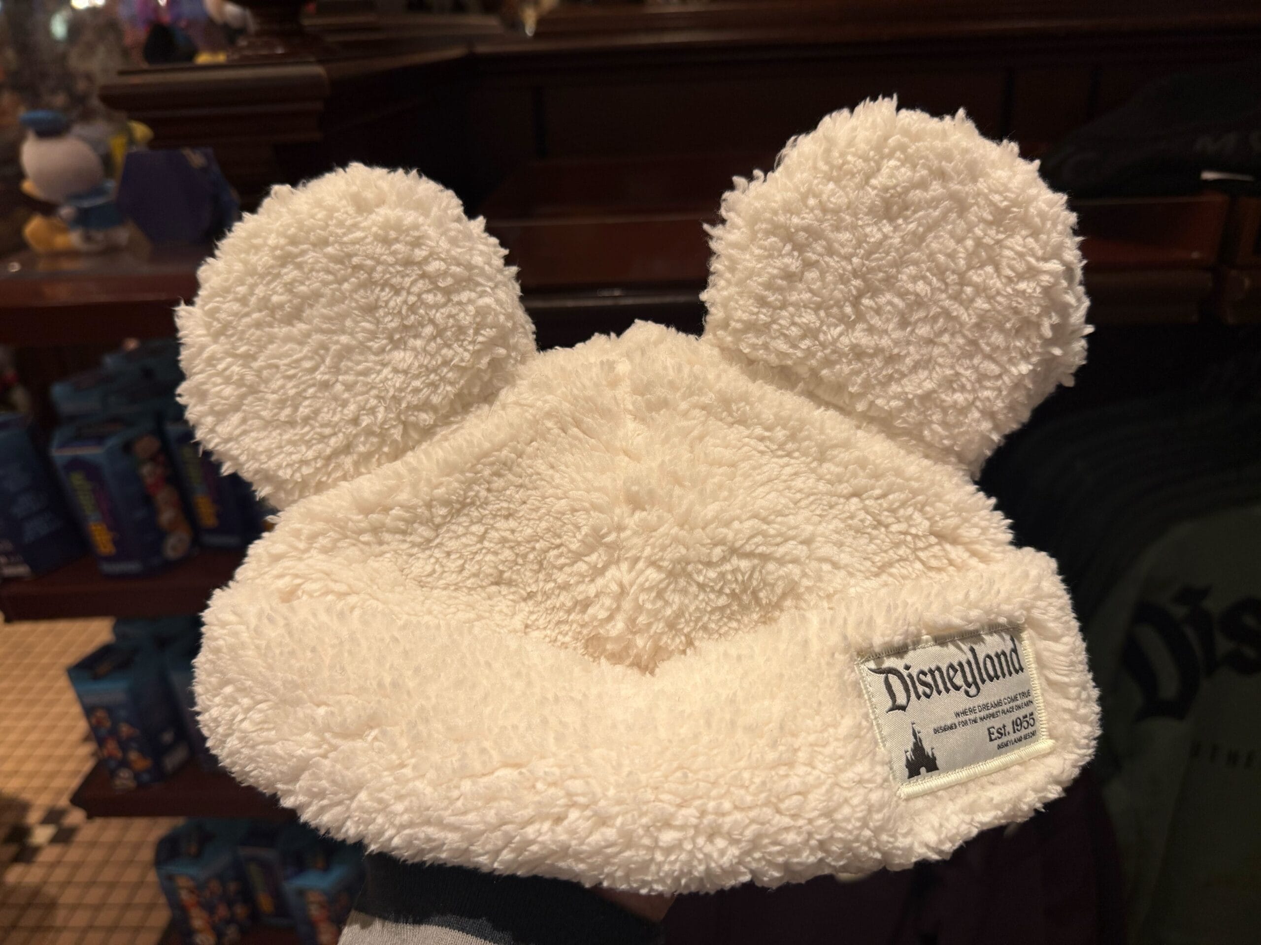 A fluffy Sherpa cap with big Mickey Mouse ears and a Disneyland patch, evoking classic park style, displayed indoors.