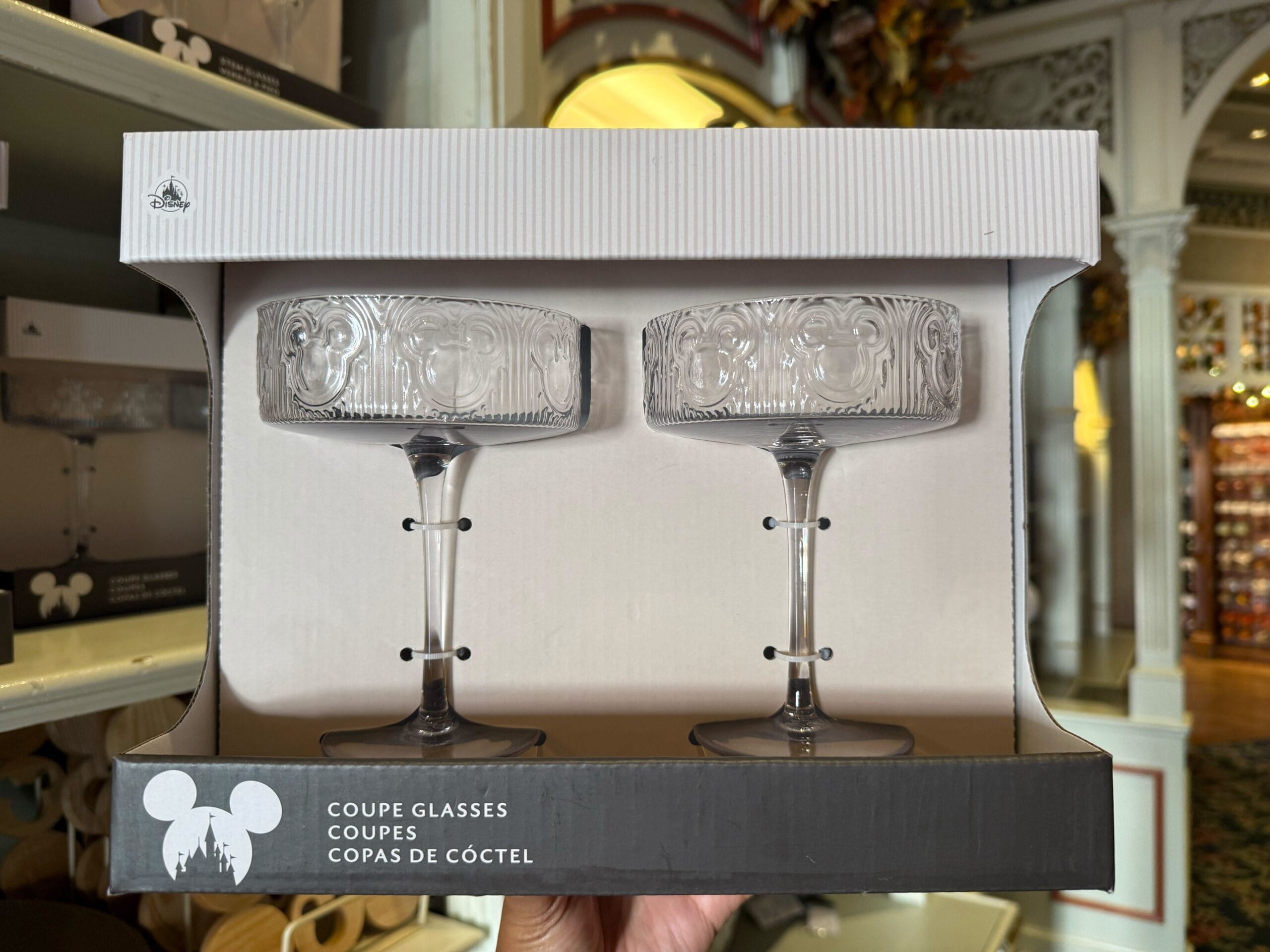 A boxed set of two coupe glasses featuring a Mickey Mouse icon, with multilingual text, reminiscent of Disney Parks merch.