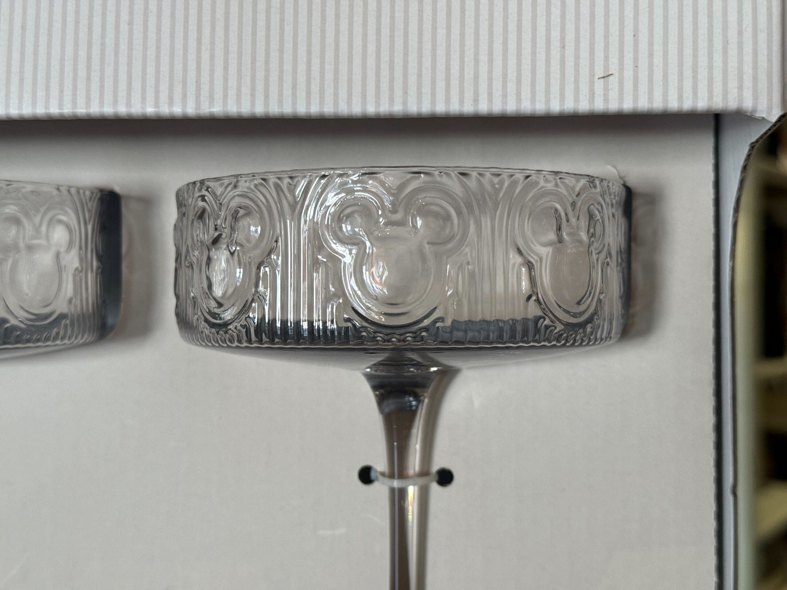 A clear stemmed glass with embossed Mickey Mouse heads around the rim, reminiscent of drinkware found at Disney Parks, on white.