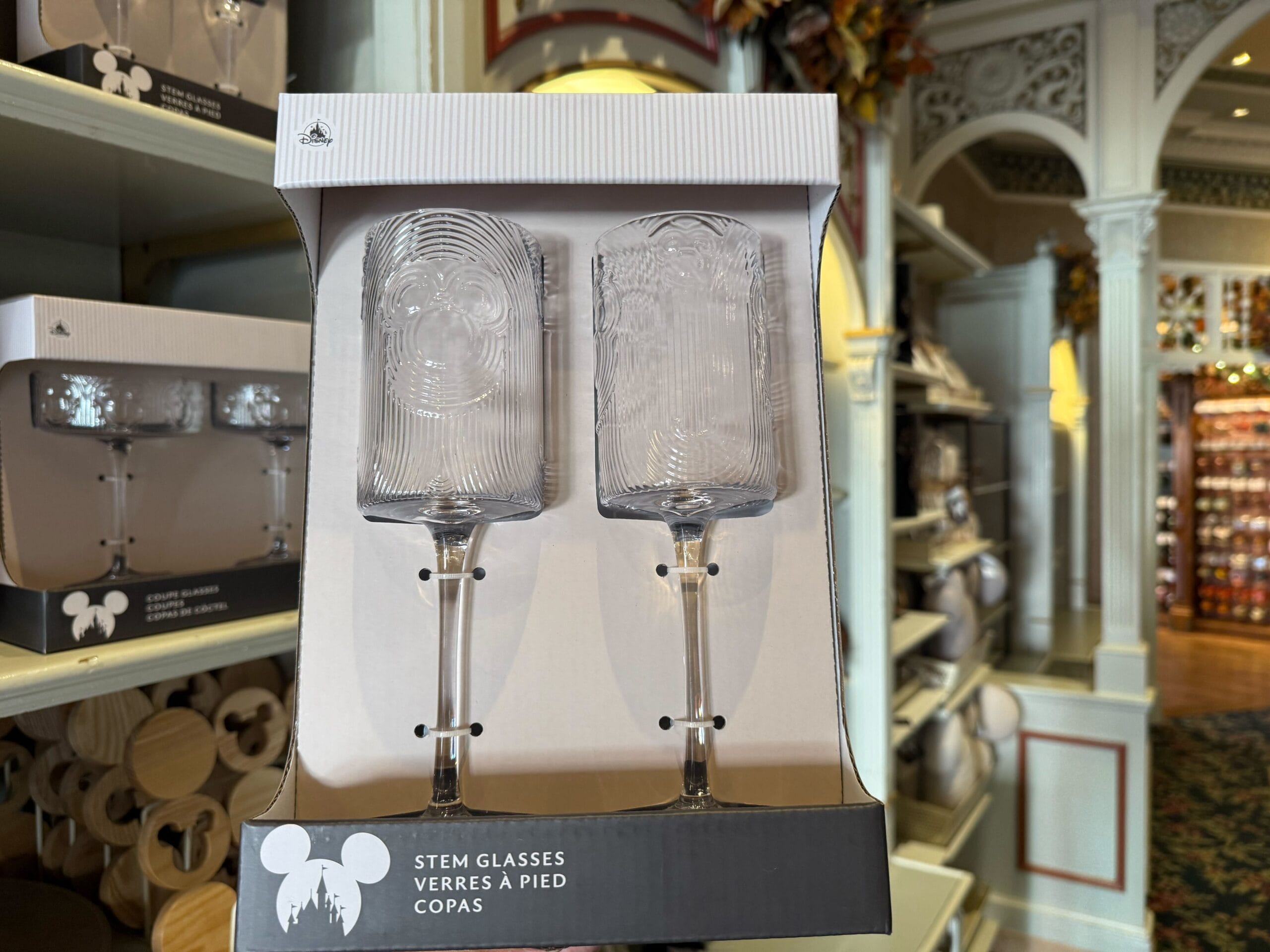 Two clear stem glasses with Mickey Mouse faces in a display box on a Disney Park store shelf—perfect park souvenir glassware.