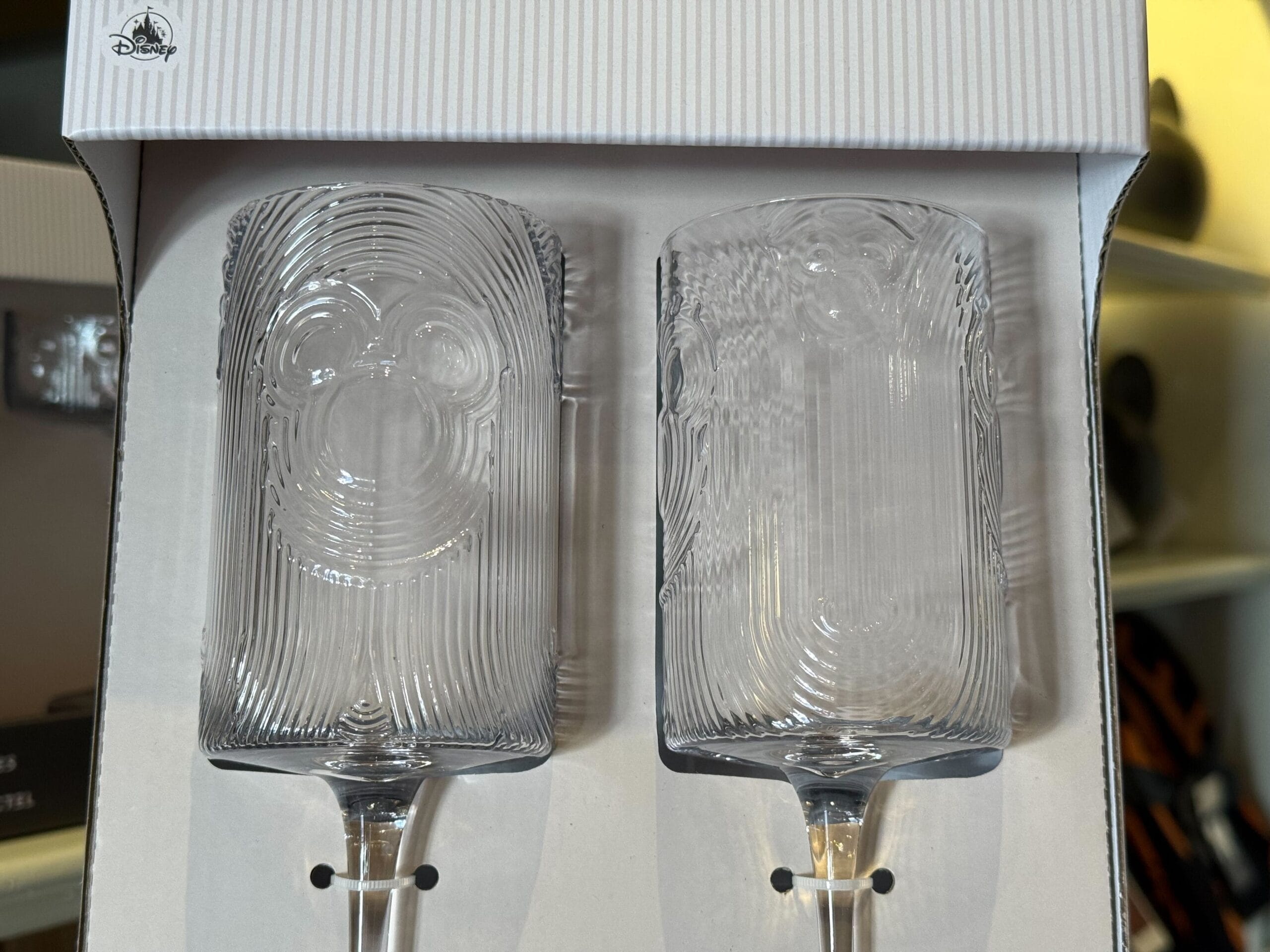Two clear glass cups featuring a subtle Mickey Mouse face, presented in a white Disney Parks box—reminiscent of park merchandise.