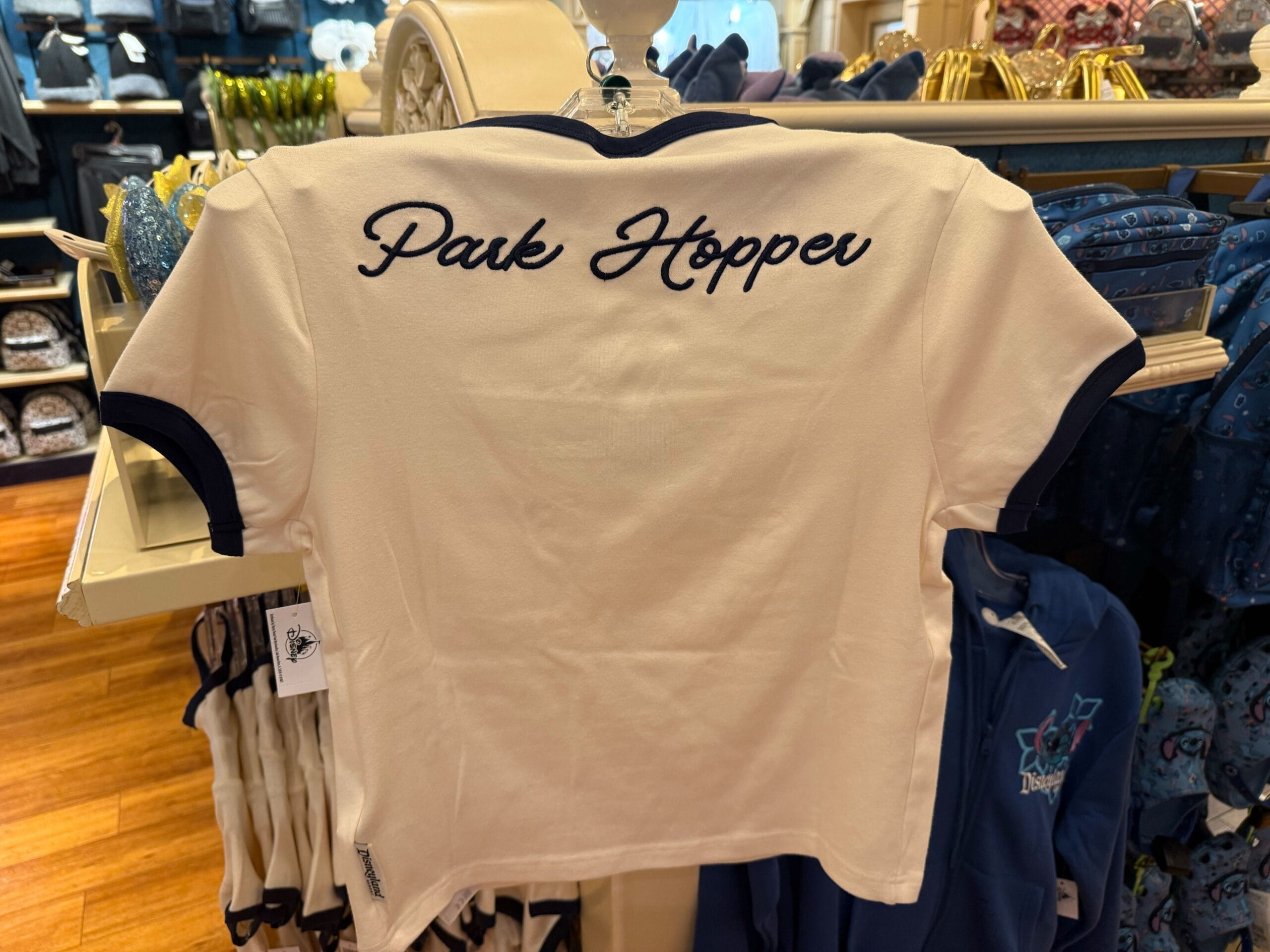 A white t-shirt with navy trim hangs on display, "Park Hopper" scripted on the back—a nod to Disney Park fans and multi-park visits.