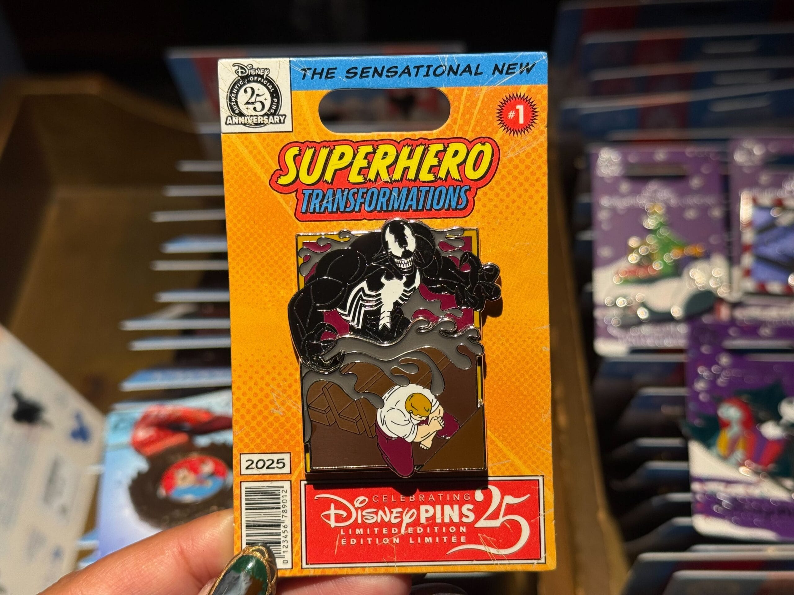 A hand displays a Disney Parks 25th anniversary "Superhero Transformations" pin with Venom and Eddie Brock.