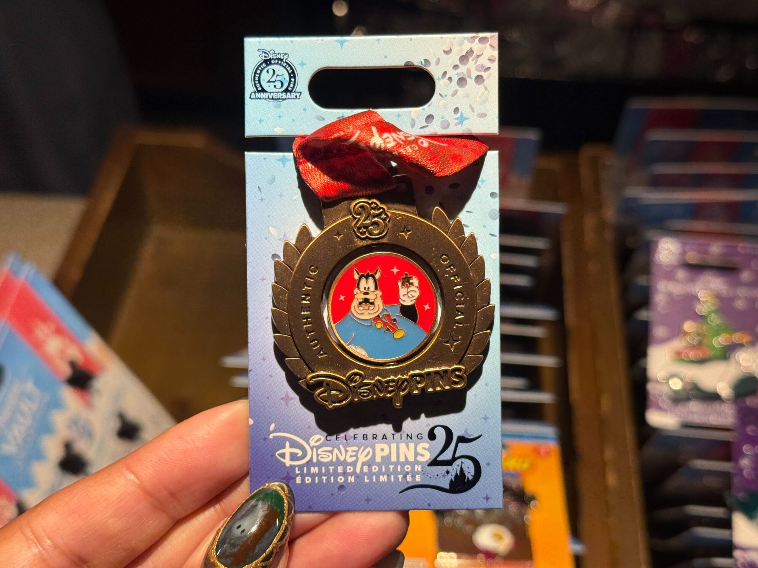 A hand displays a Disneyland 25th anniversary Pin Tuesday pin with Pete on a red background surrounded by a bronze medal.