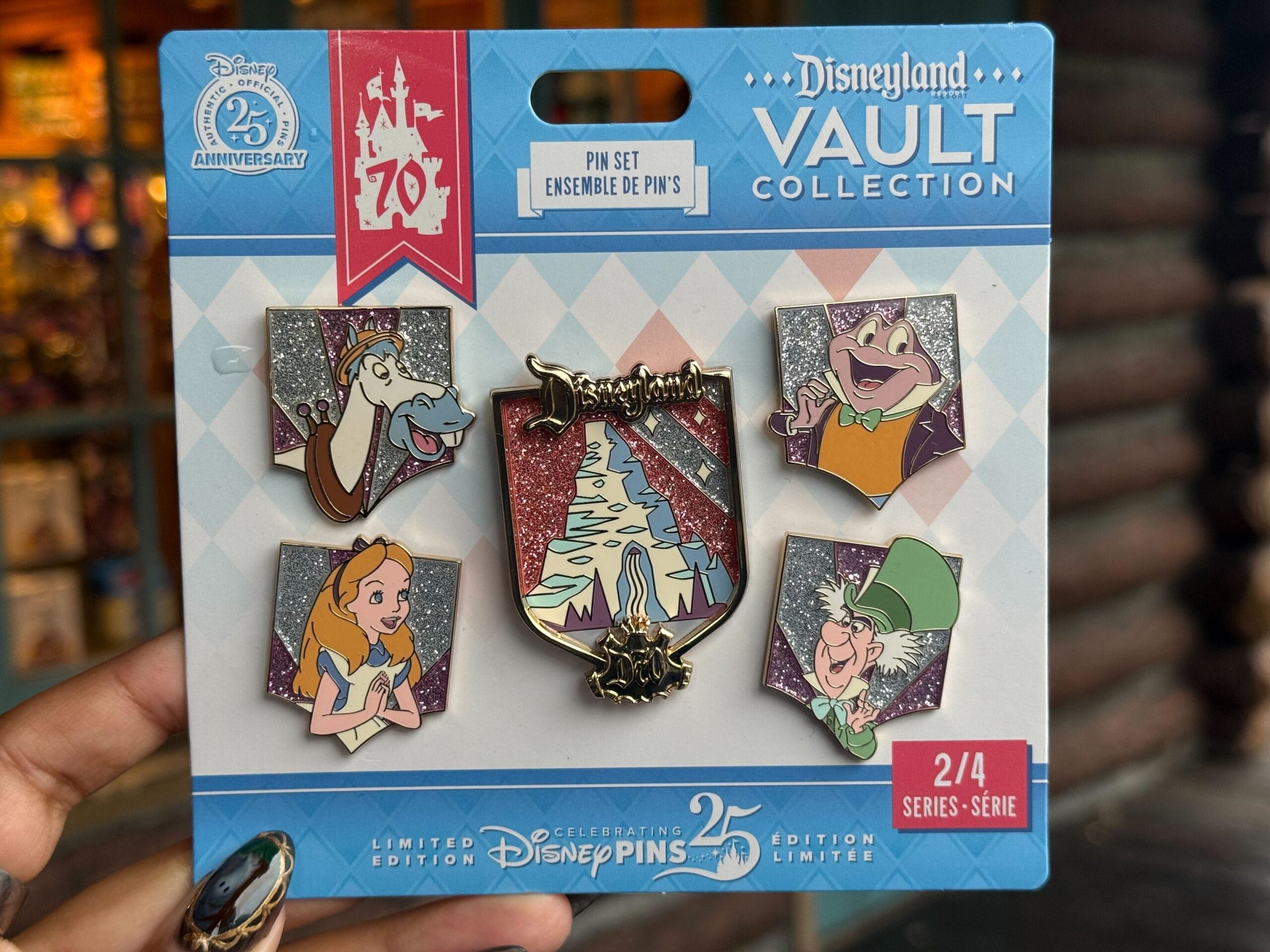 A hand displays five vibrant Disneyland Vault Collection pins for Pin Tuesday, featuring Cyril Proudbottom, Mr. Toad, Alice, the Mad Hatter, and Matterhorn Bobsleds against glittery backgrounds.