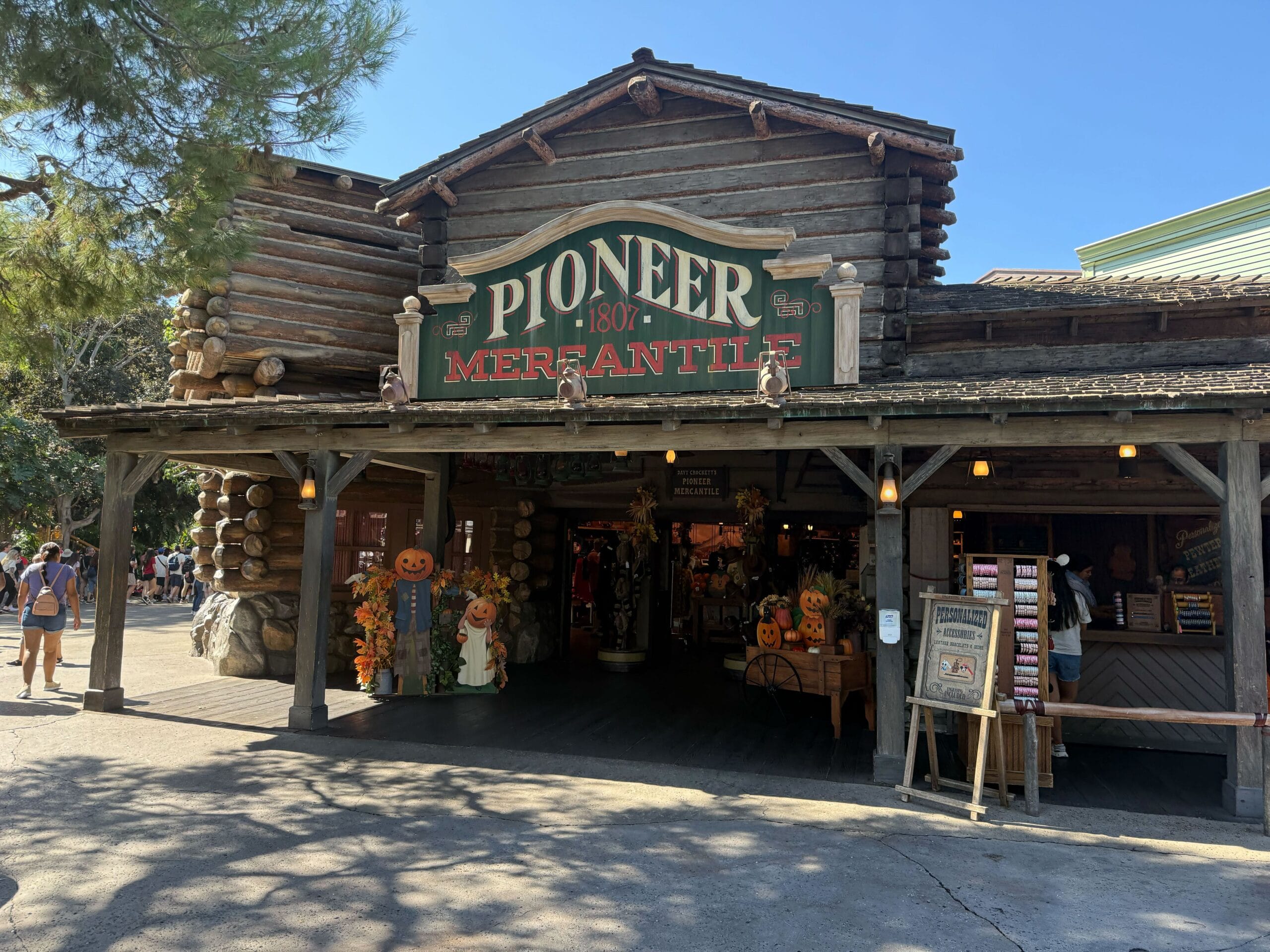 A rustic wooden shop labeled "Pioneer Mercantile," adorned with fall decor and a Cowboy Boots Shirt under a clear sky.