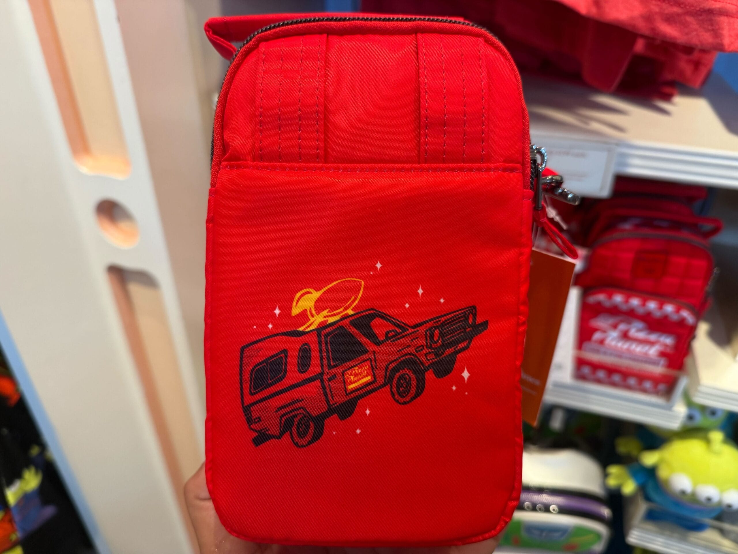 A small red bag with a graphic of a pizza delivery truck wearing a yellow hat, reminiscent of whimsical Disney park merchandise.