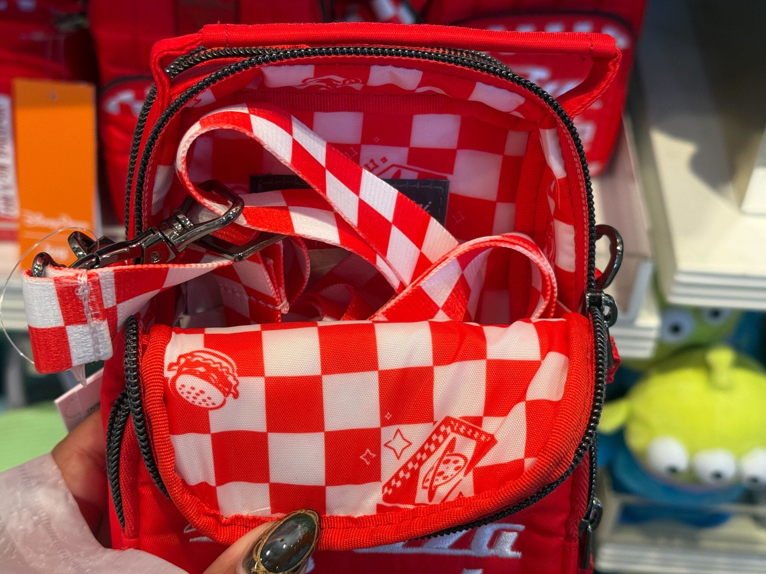 The bag’s red and white checkered interior features burgers and fries, unzipped like a Disney lunch tote, showing straps inside.