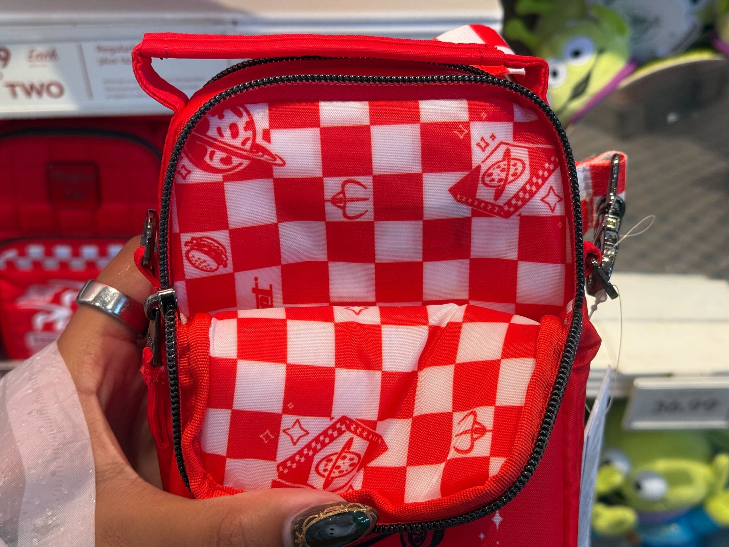 A small red and white checkered Pizza Planet bag, held open by someone in a Disney park store, referencing Toy Story.