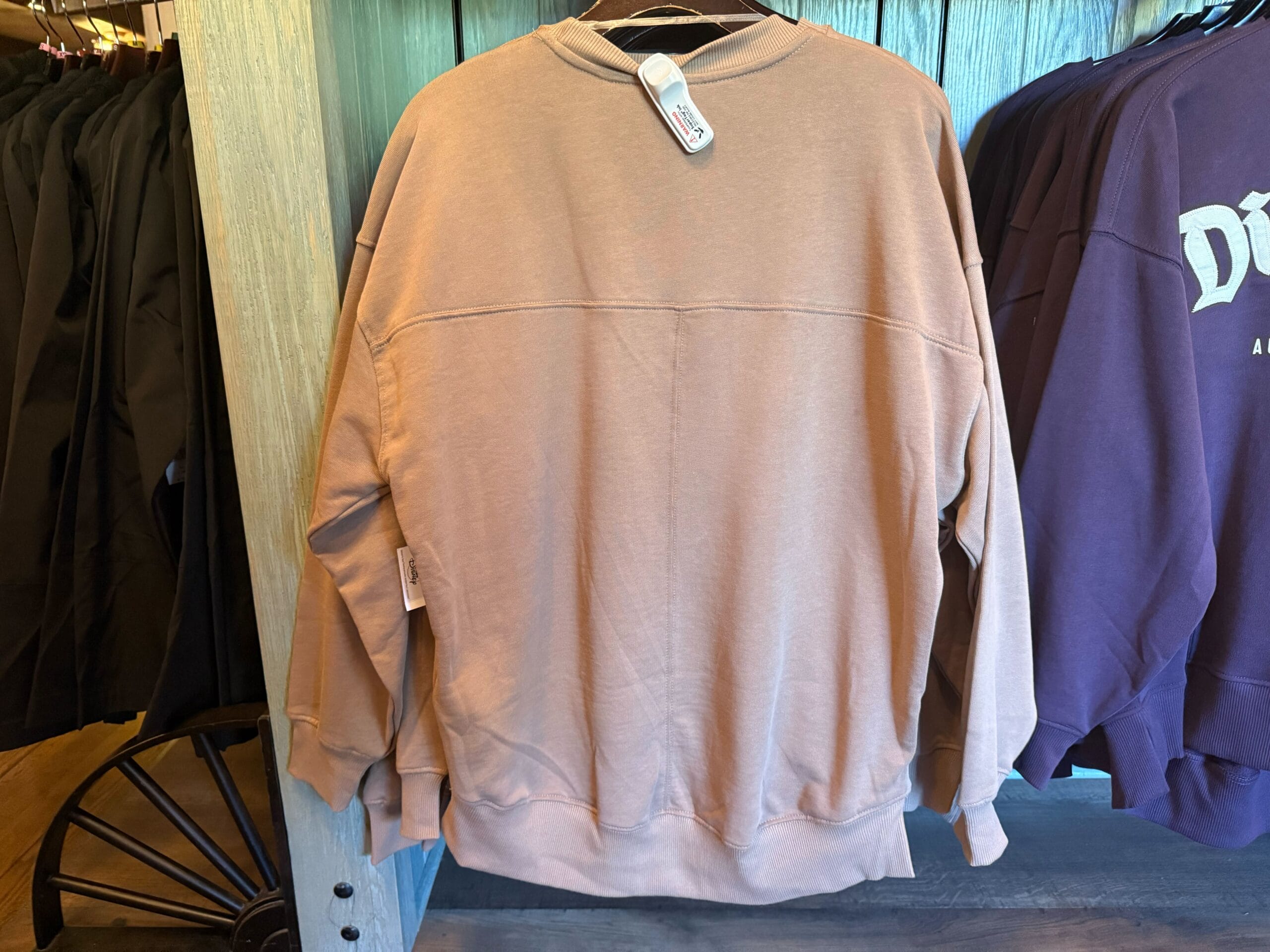 Light brown Logo Sweatshirt hanging on a rack, displayed with other clothing in a store.