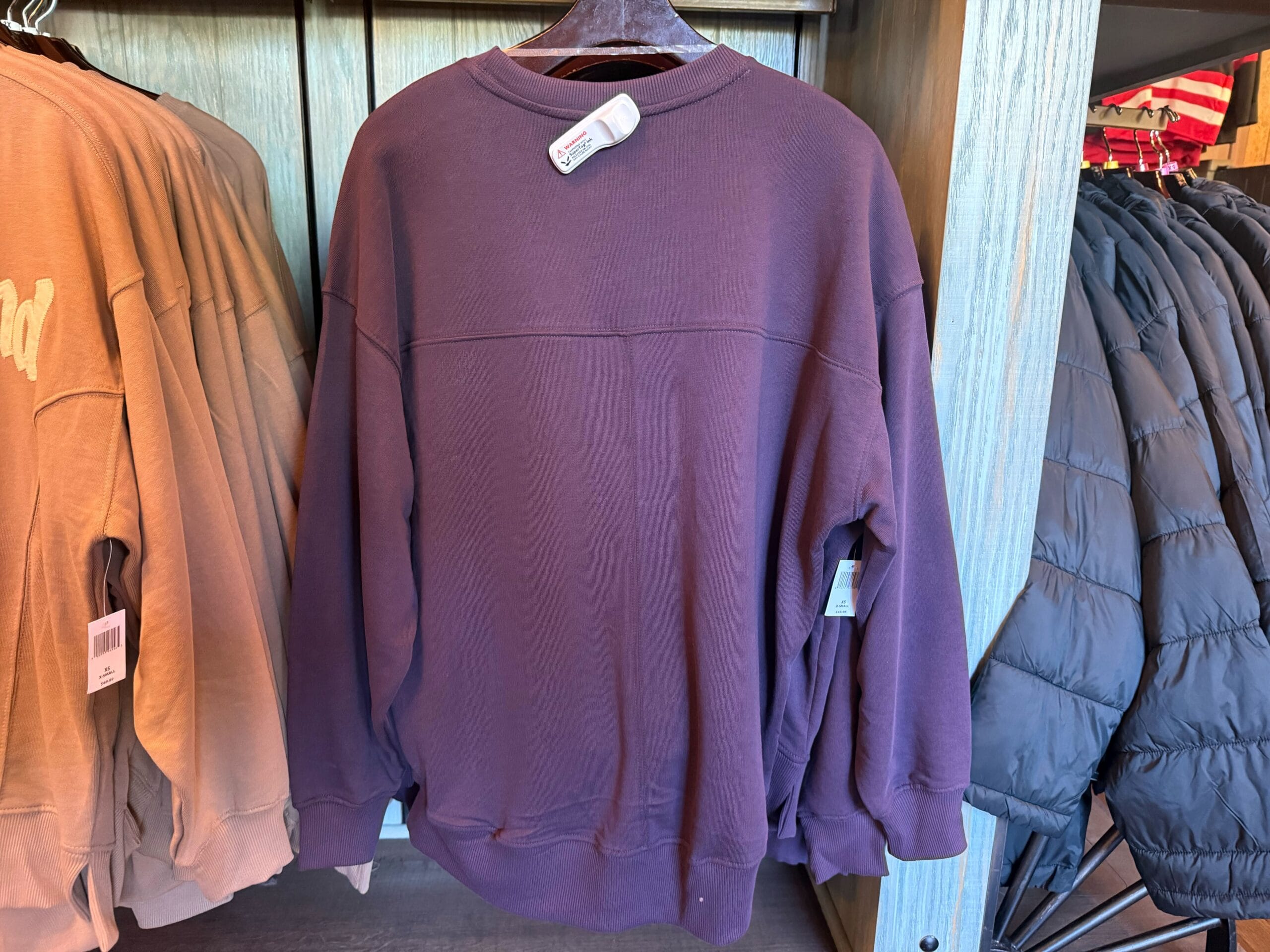 A plain purple logo sweatshirt on a hanger, displayed in a clothing store between tan and black jackets.