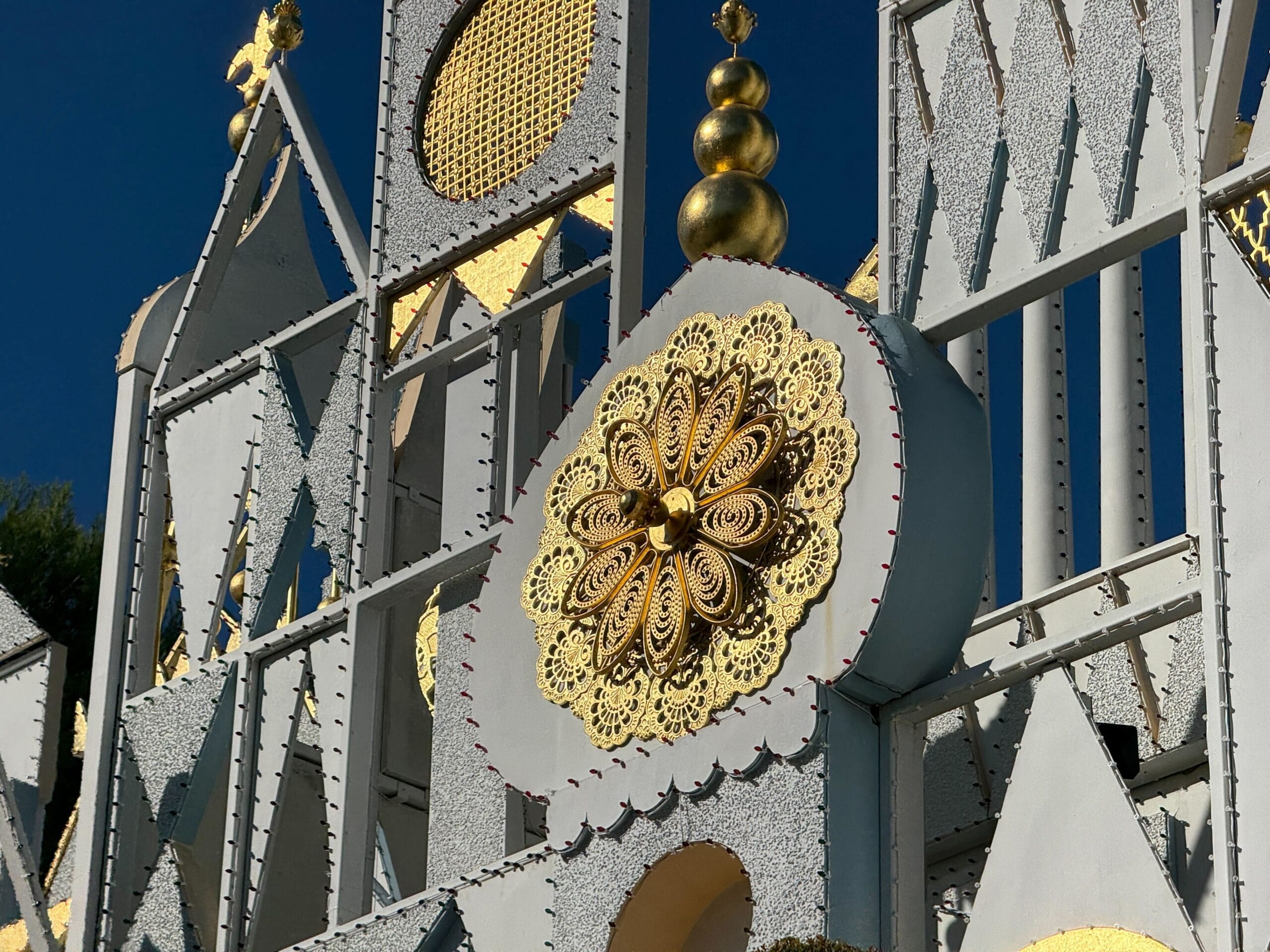 Close-up of a gold and silver facade with intricate patterns, reminiscent of Disneyland's it's a small world, under a clear blue sky.