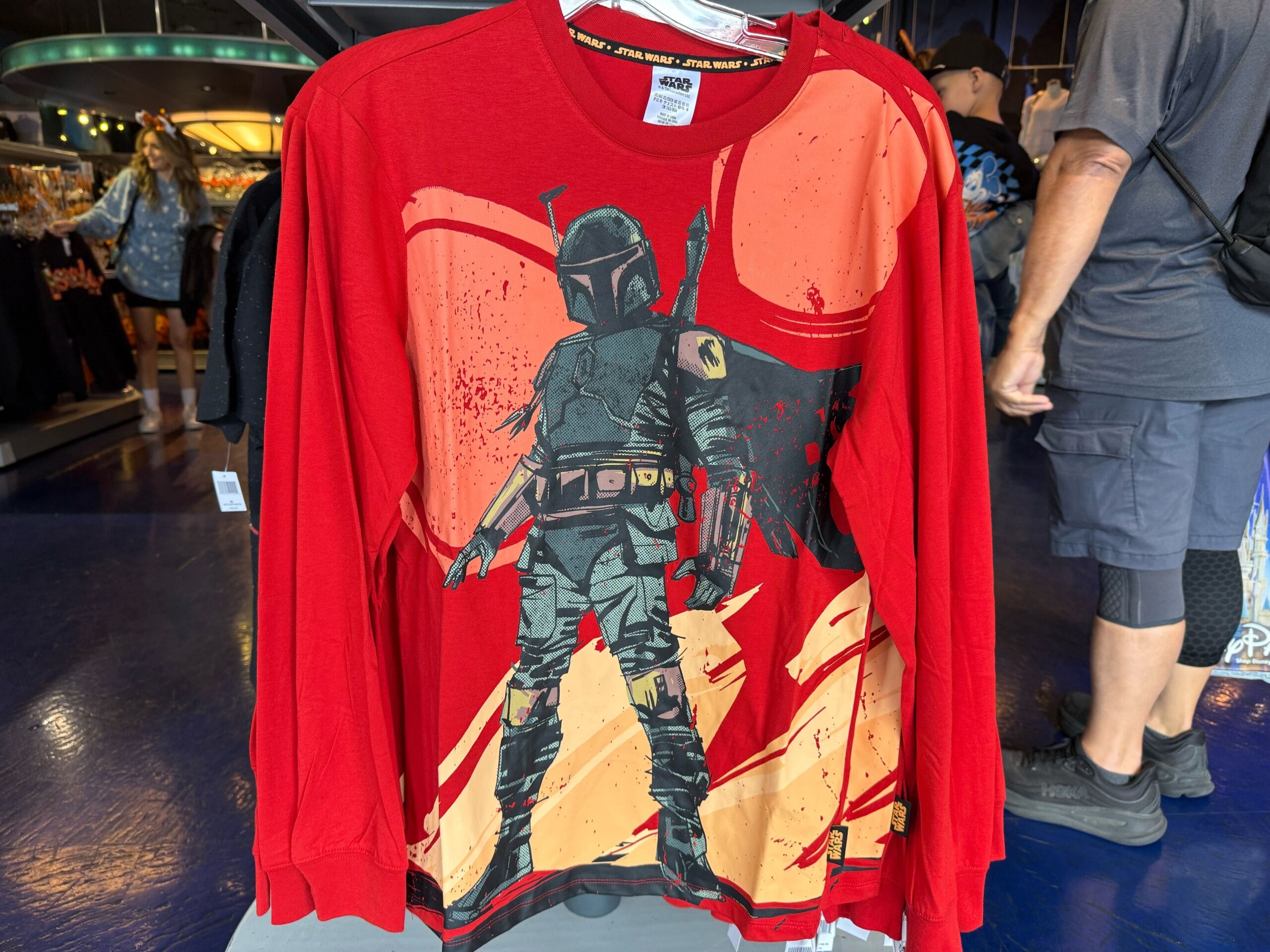 Red long-sleeve Star Wars shirt with Boba Fett graphic, displayed in a Disney park shop—no castle in view to compare.