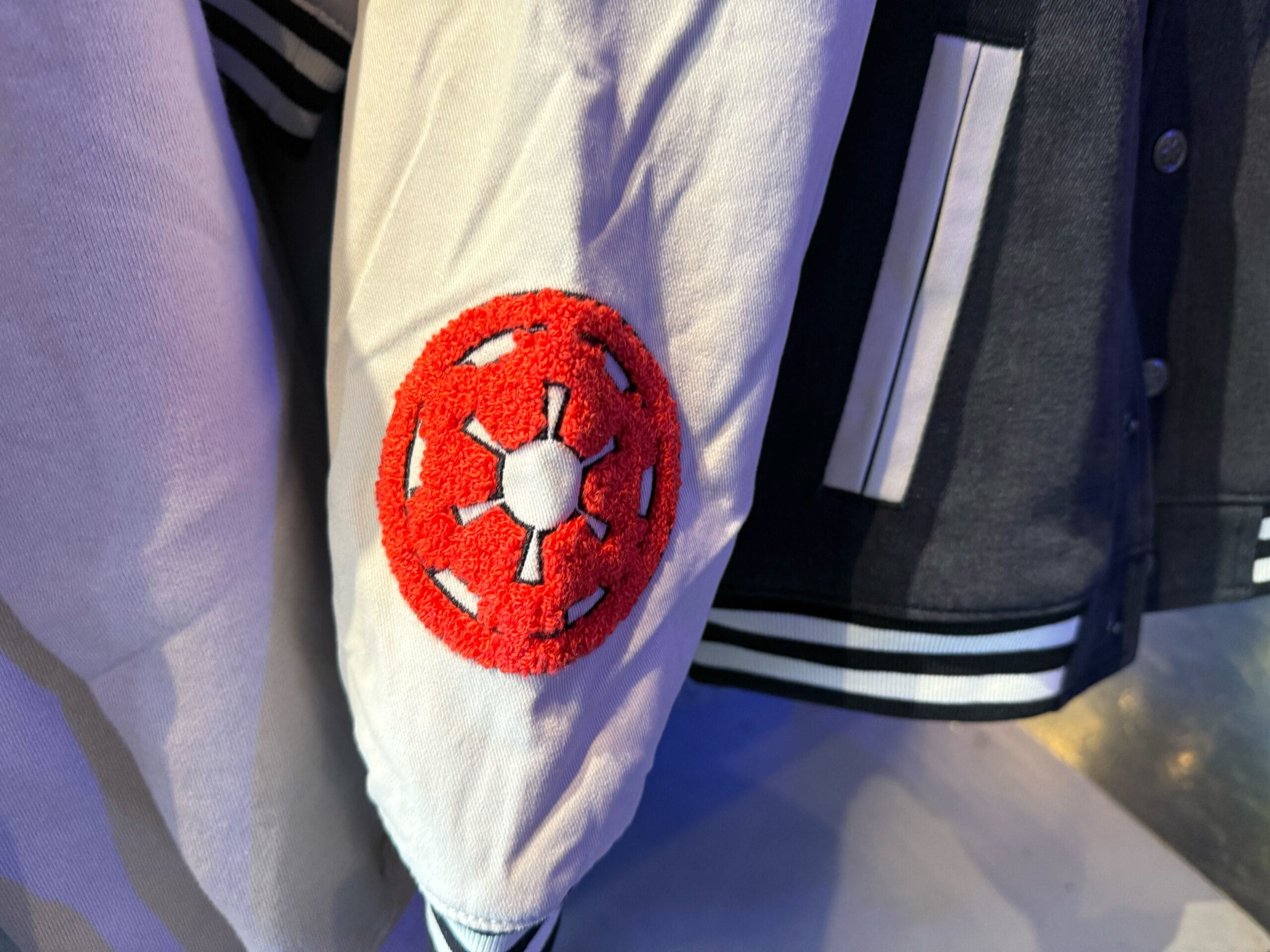 White sleeve of a black and white varsity jacket with a red Star Wars Galactic Empire patch, seen at a Disney park—no castle shown.
