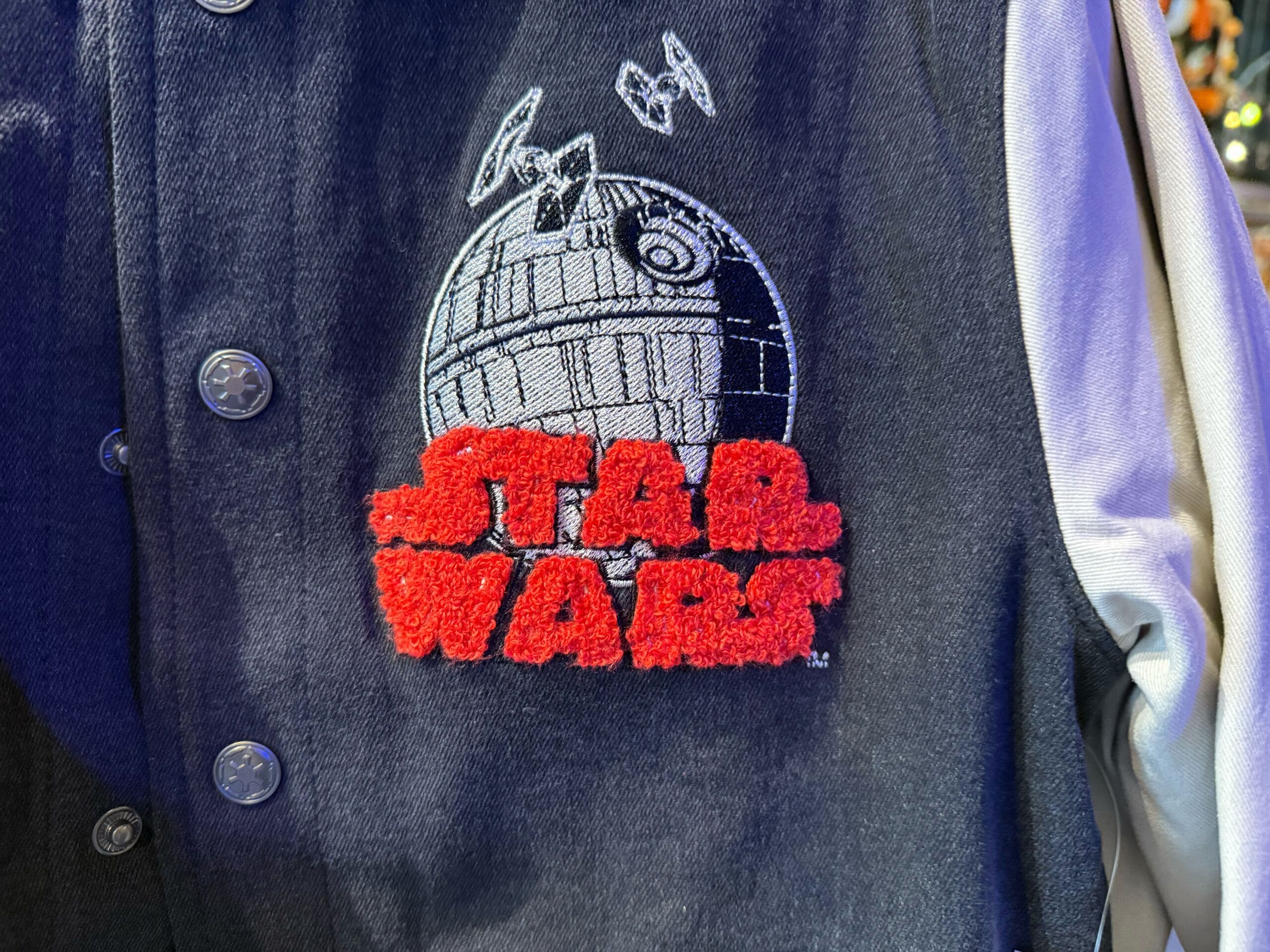 Close-up of a jacket featuring a Death Star and TIE fighters patch, with bold red "Star Wars" text, seen at Disney Parks.