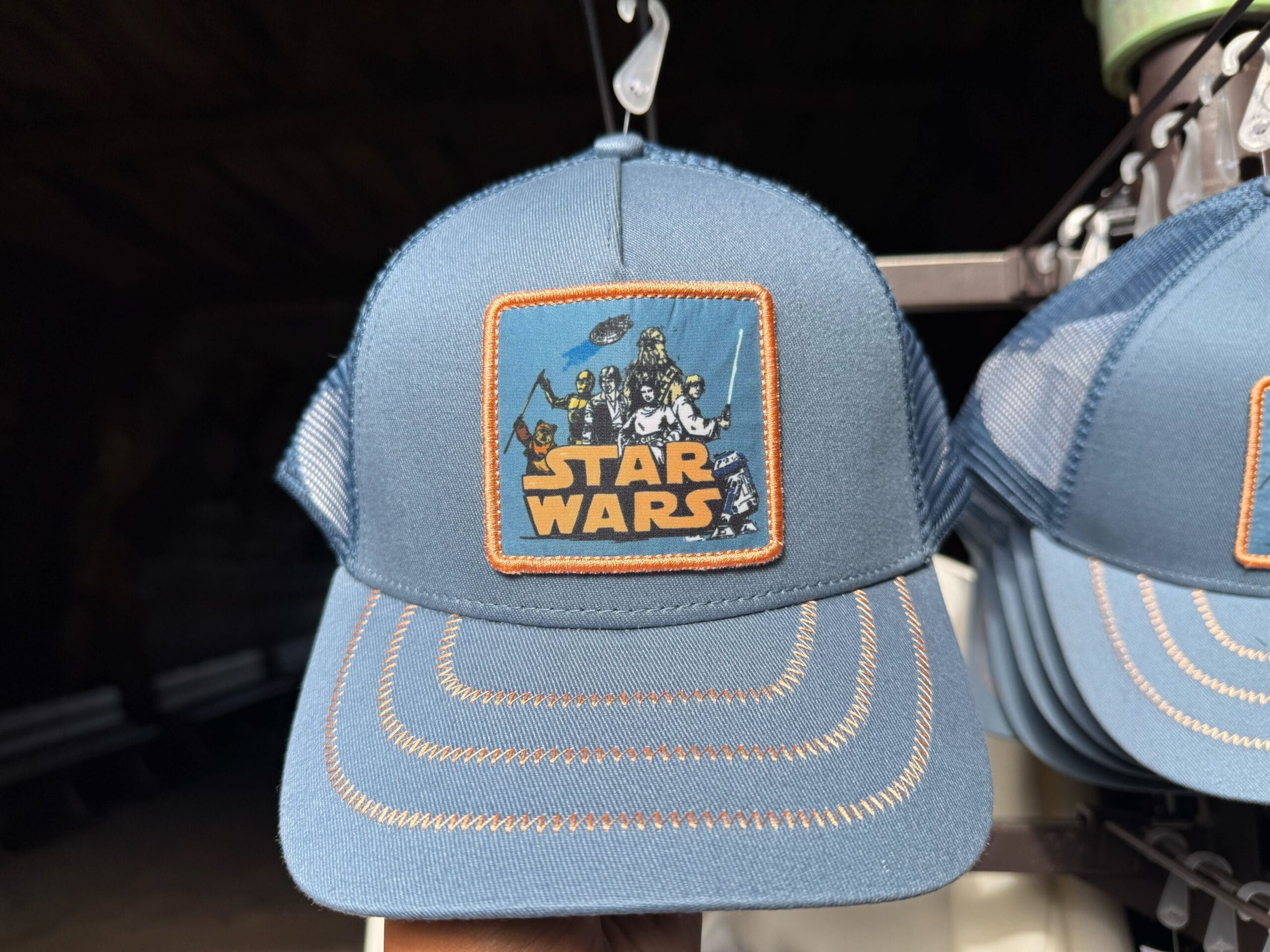 A blue trucker hat with a vibrant Star Wars patch displaying Darth Vader and other characters, seen at Disney Parks merchandise shops.