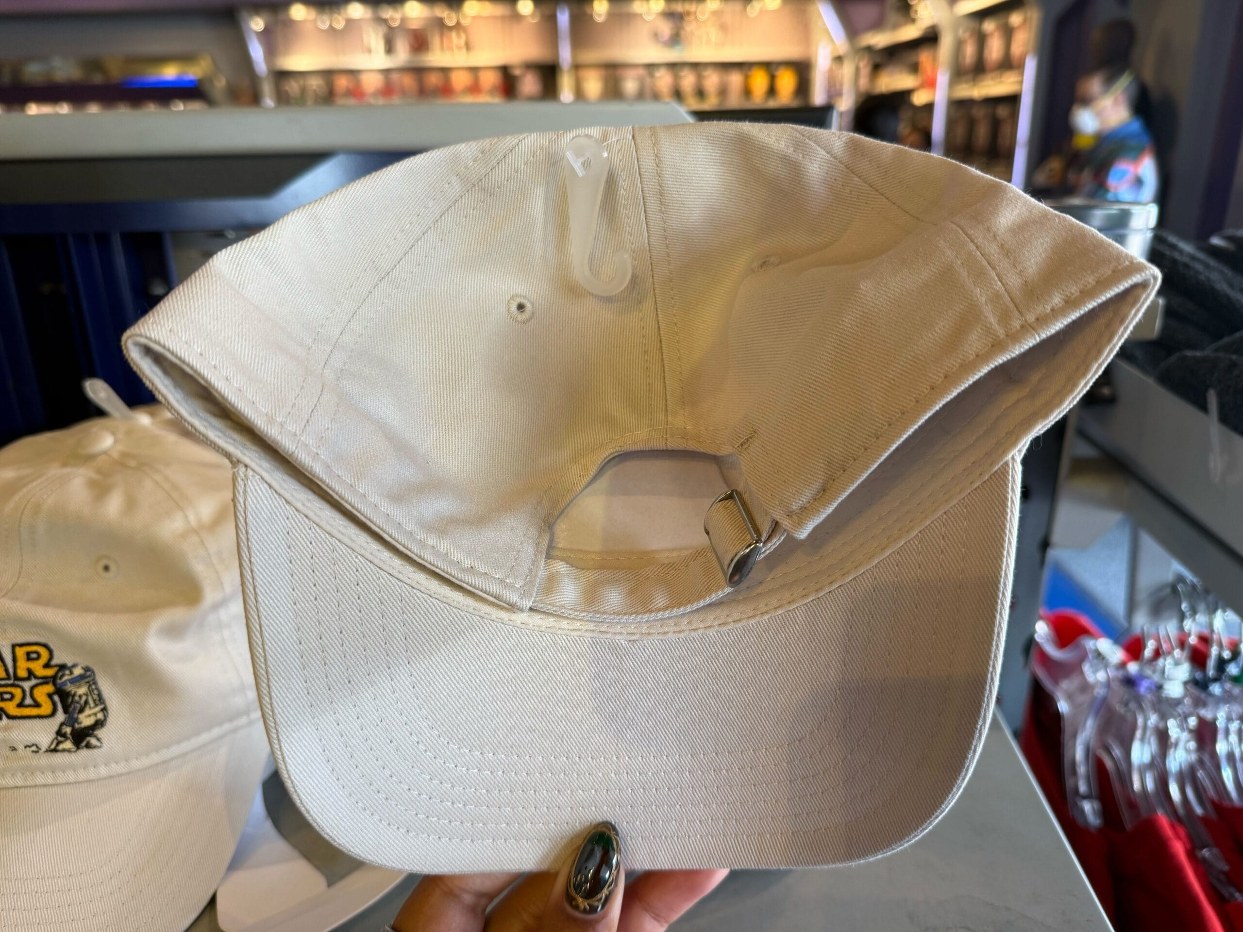 Beige cap turned inside out, exposing metal strap and interior stitching—great Star Wars accessory, seen in Disney Parks shops.