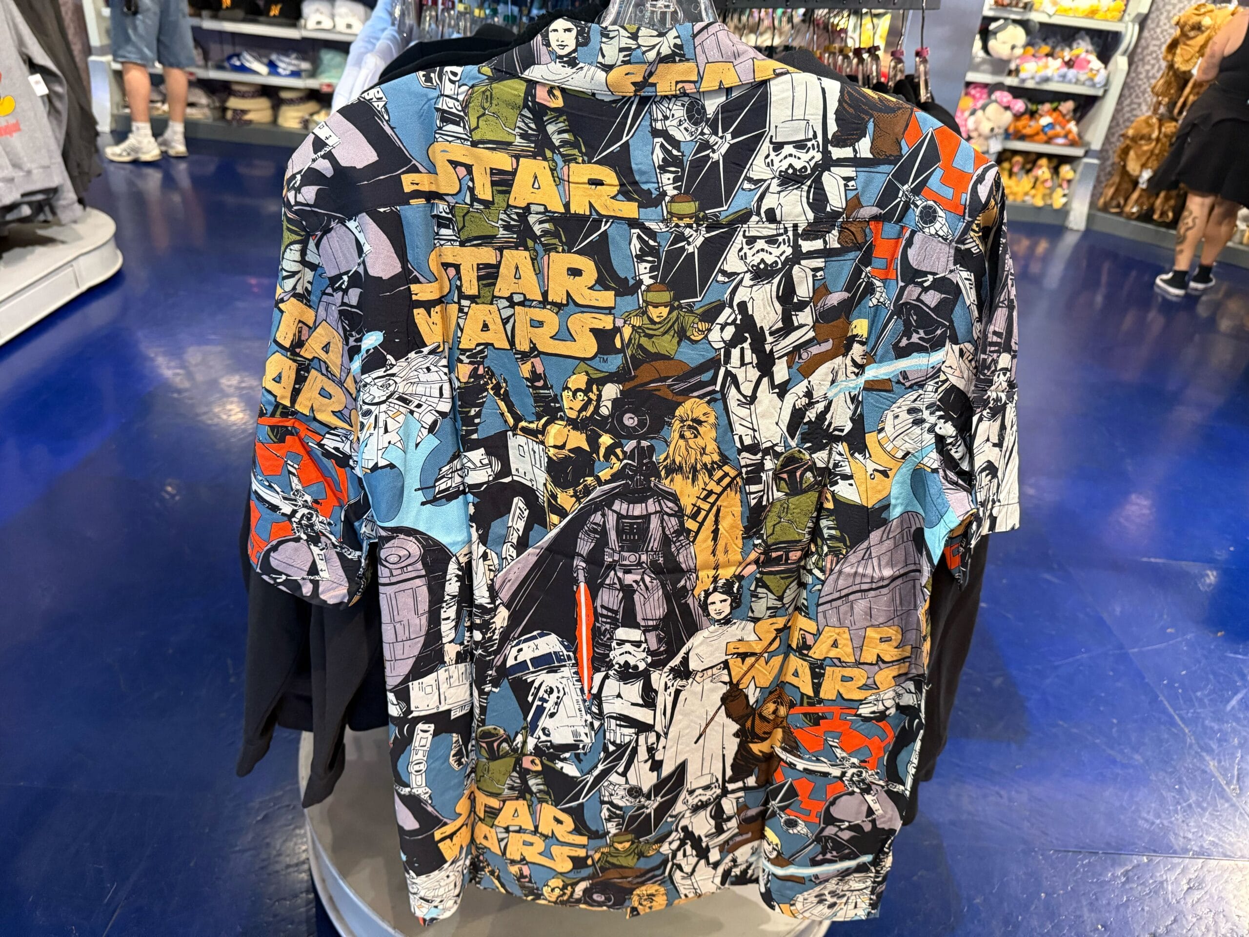 A Star Wars shirt with vibrant characters like Boba Fett and Darth Vader, shown on blue flooring—not modeled at a Disney park castle.