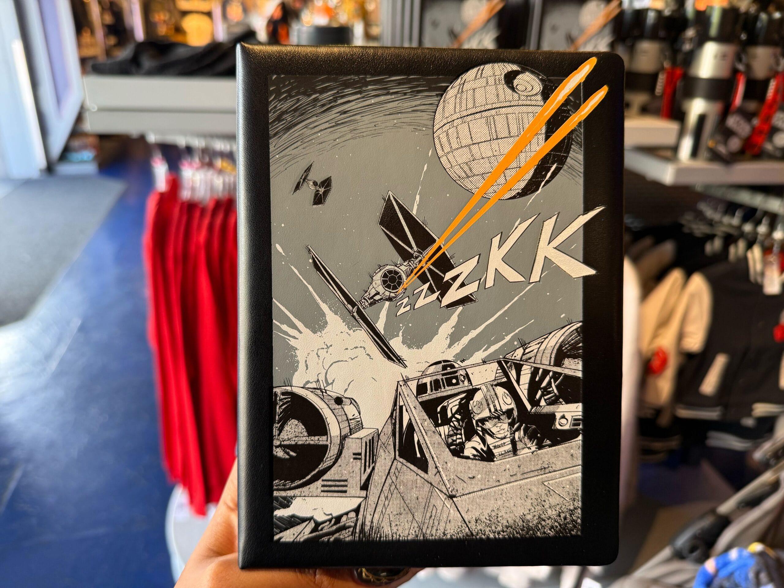 A hand holds a Star Wars notebook featuring Boba Fett and a Death Star battle, reminiscent of Disney Parks’ themed merchandise.