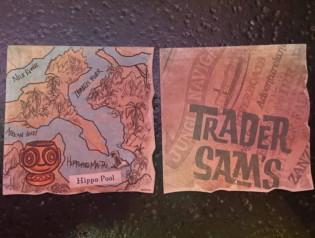 A pair of coasters designed like pieces of a torn map. The left coaster specifies landmarks along rivers with a Hippopotomaitai mug in the corner. The right coaster has the Trader Sam's logo over an Adventureland themed pattern.