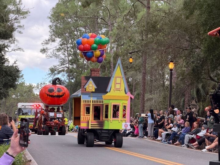 A parade float of the "Up" house with bright balloons glides past crowds, evoking Pixar charm in a lively Disney parks parade.