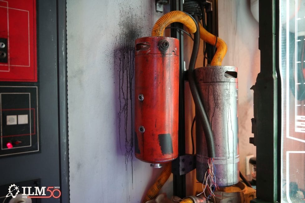 Two large, weathered metal cylinders with yellow cables appear in a Star Wars setting at a Disney park near themed control panels.