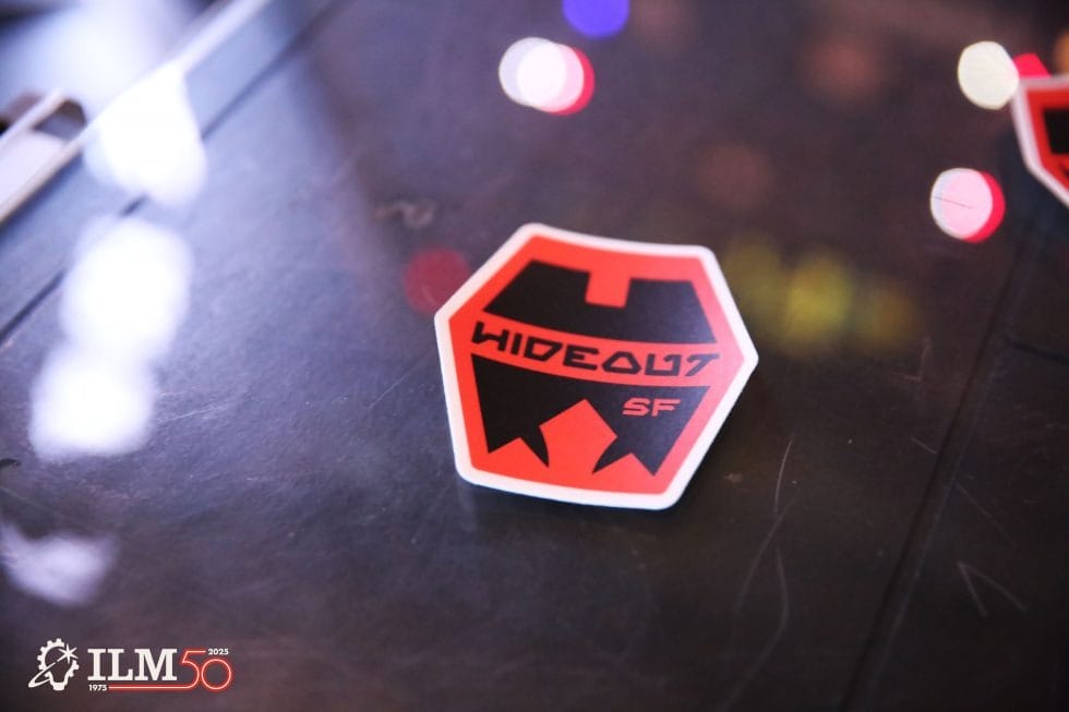 A red and black "HIDEOUT SF" sticker with the ILM 50 logo on a surface in the Lucasfilm Lounge, not a Disney park castle.