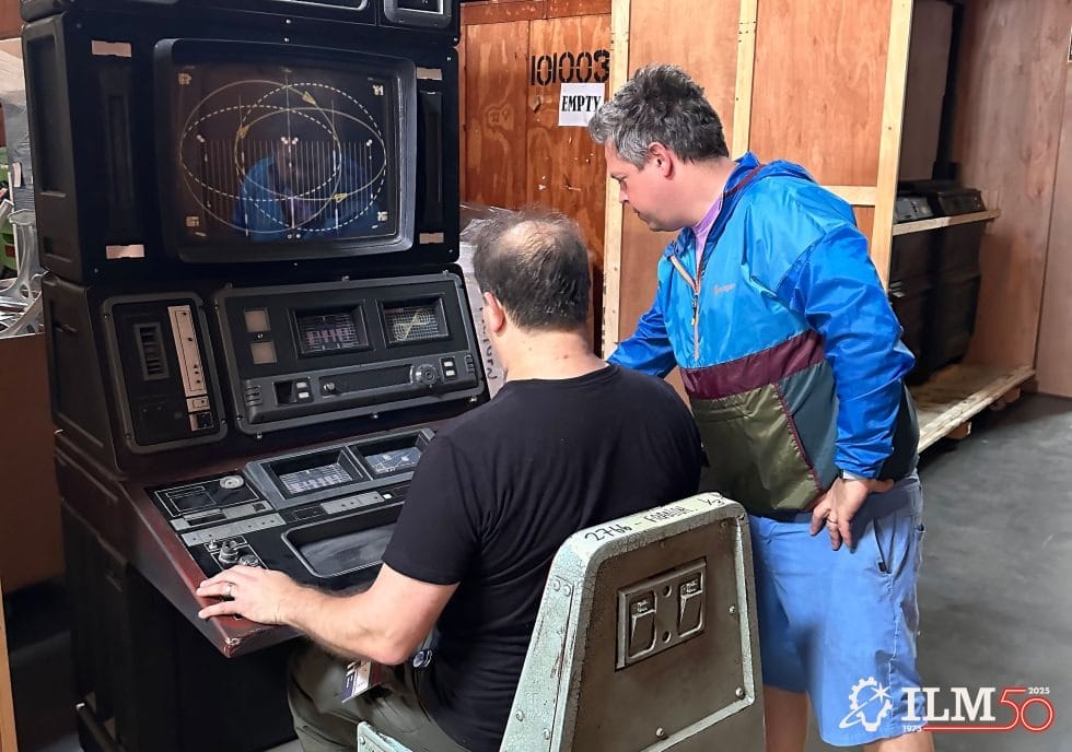 Two men use a retro computer console with several monitors in a lounge, similar to Disney parks’ themed tech displays.