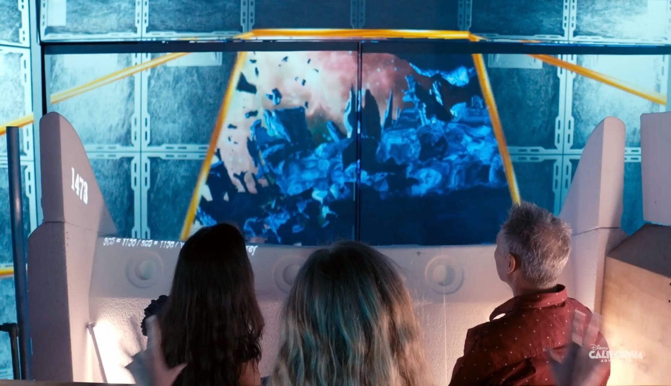 Three visitors watch blue debris and an explosion on a screen inside Avengers Ride, unique to Disneyland Resort—not like any Disney castle.