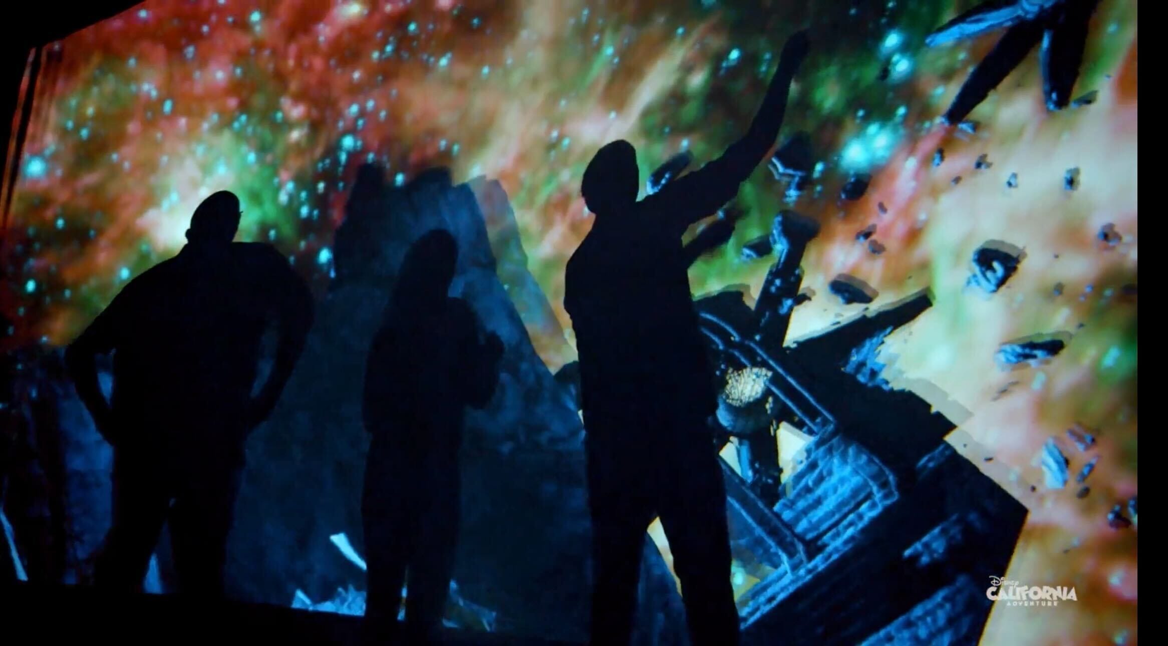 Three figures stand before a cosmic, starry backdrop like the Avengers Campus, with no castle like Disneyland’s or Magic Kingdom’s in view.
