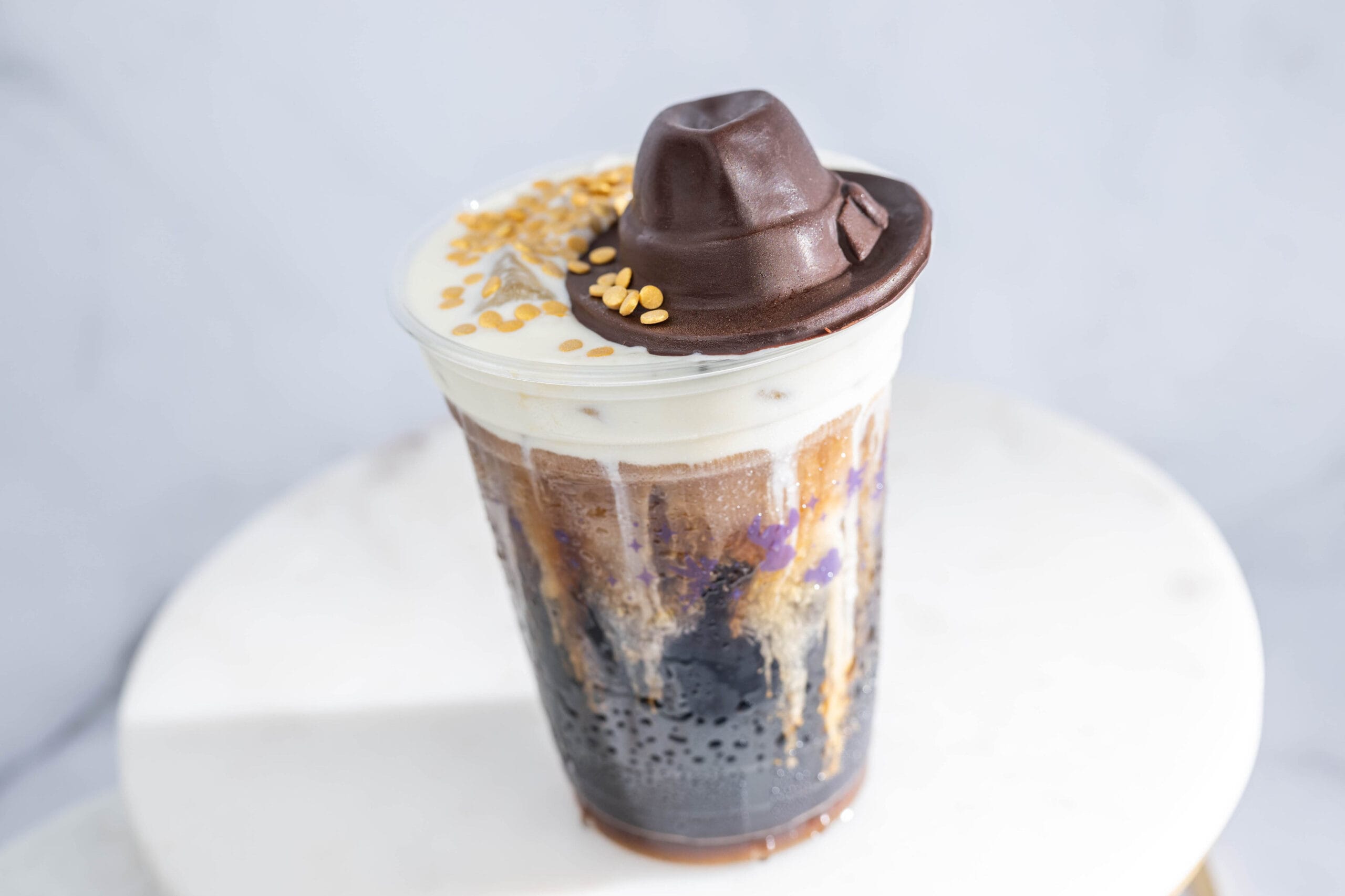 Iced Cold Brew with cream, black jelly, a chocolate hat, and yellow crunch—perfect after Indiana Jones at Hollywood Studios.
