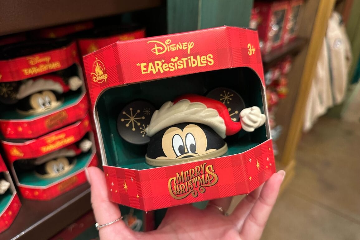 دستی که یک اسباب‌بازی کریسمس میکی ماوس «EARresistibles» دیزنی را در بسته‌بندی قرمز و شاد نگه داشته است؛ این محصول در پارک‌های دیزنی سراسر جهان یافت می‌شود.