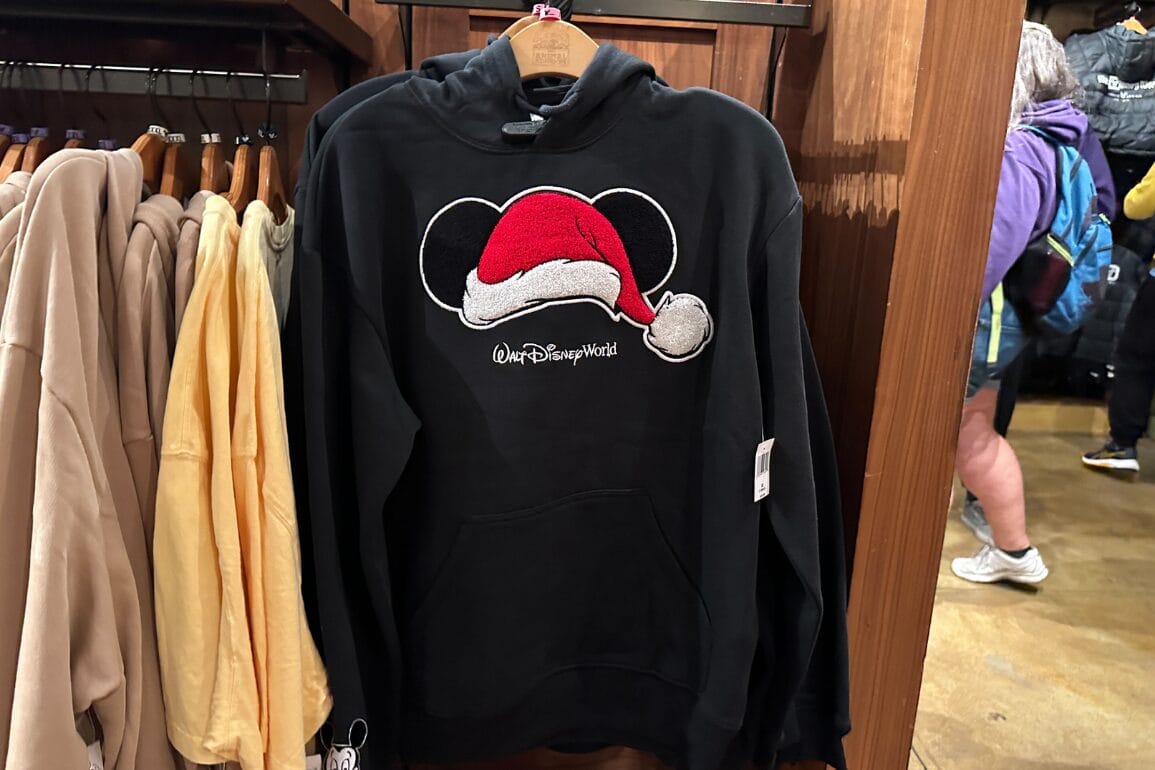 هودی مشکی شاد دیزنی ورلد با طرح گوش‌های میکی ماوس در کلاه سانتا، در کنار دیگر کالاهای تعطیلات در فروشگاه پارک به نمایش گذاشته شده است.