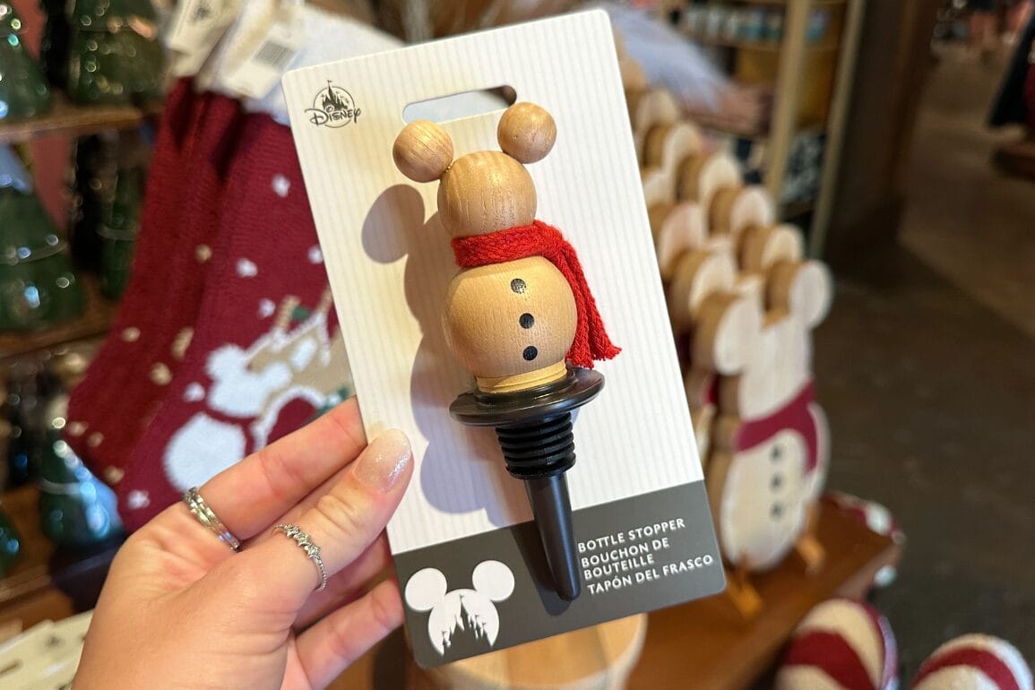 دستی که یک درپوش بطری دیزنی ورلد به شکل آدم‌برفی با گوش‌های میکی و شال‌گردن قرمز را نگه داشته است، گزینه‌ای عالی برای سوغاتی‌های پارک.