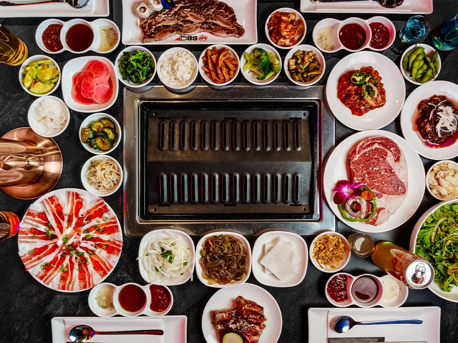 A table set for Korean BBQ at CityWalk, with raw meats, sides, and an empty grill—no Disney castle like those at Disney parks.